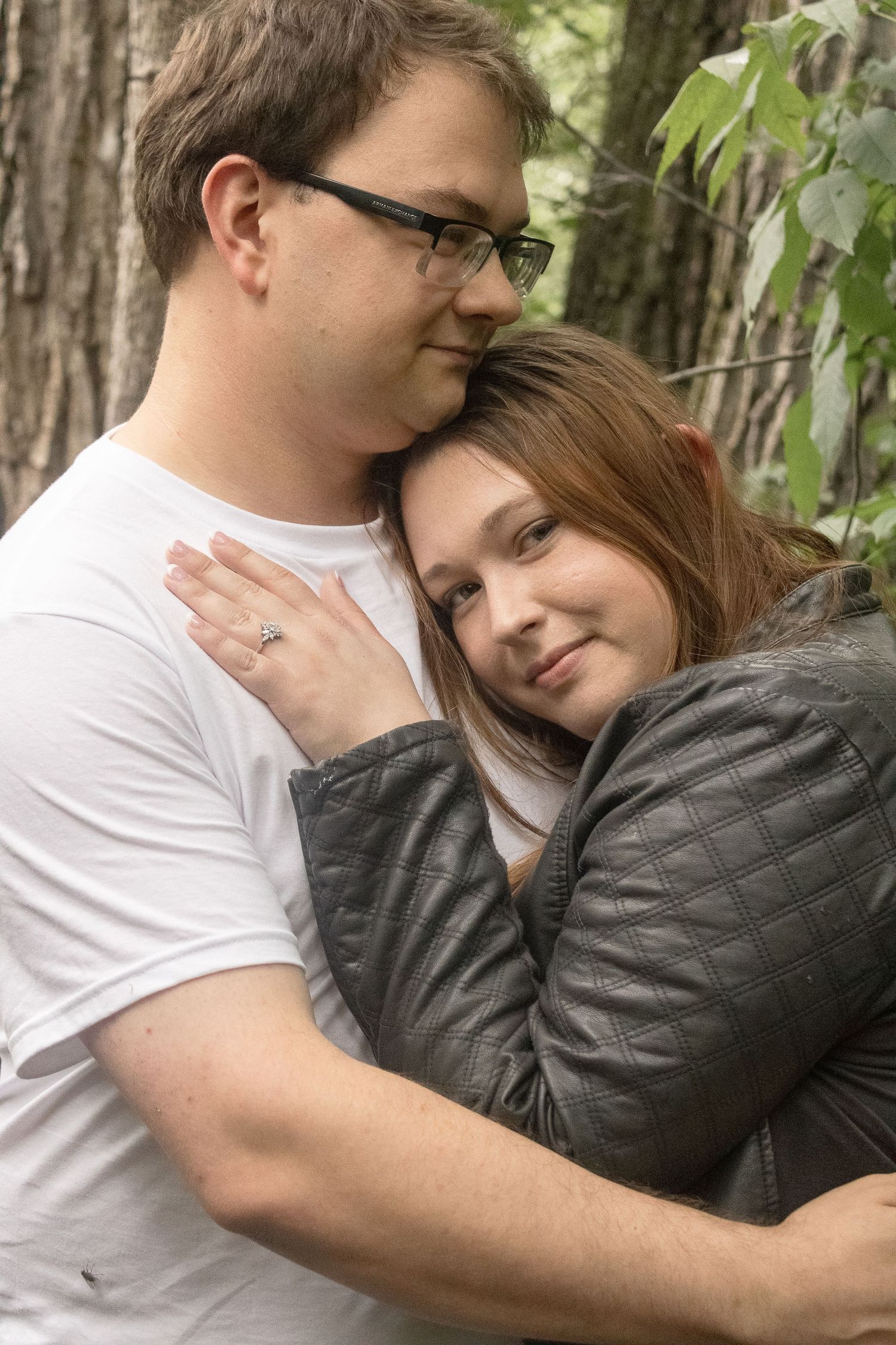 A romantic couple embraces in a forest setting with soft natural lighting creating an intimate moment.