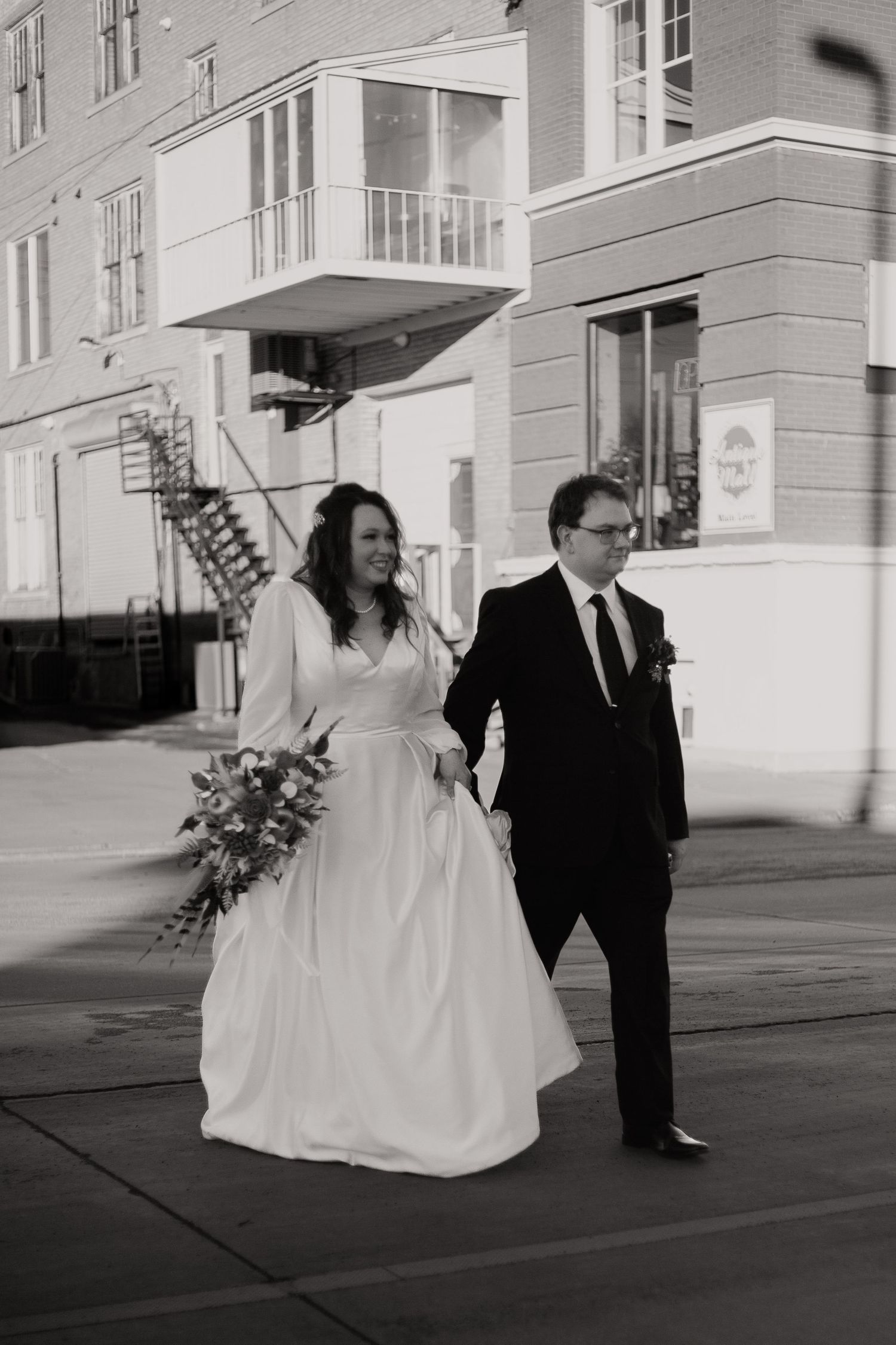 Black and white wedding photograph showing couple walking together on city sidewalk.