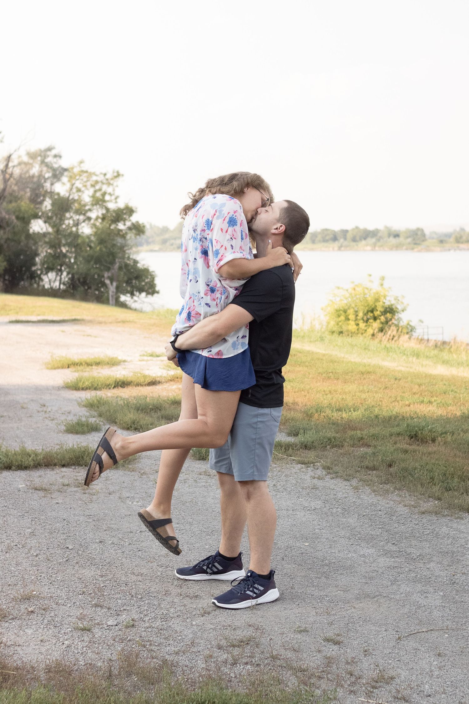 A joyful couple embraces by a lake, with one person lifted off the ground.