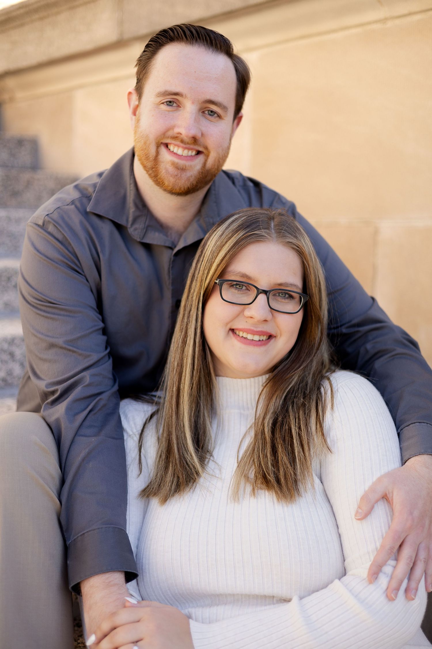 A sweet portrait of a couple sitting together outdoors near stone architecture.