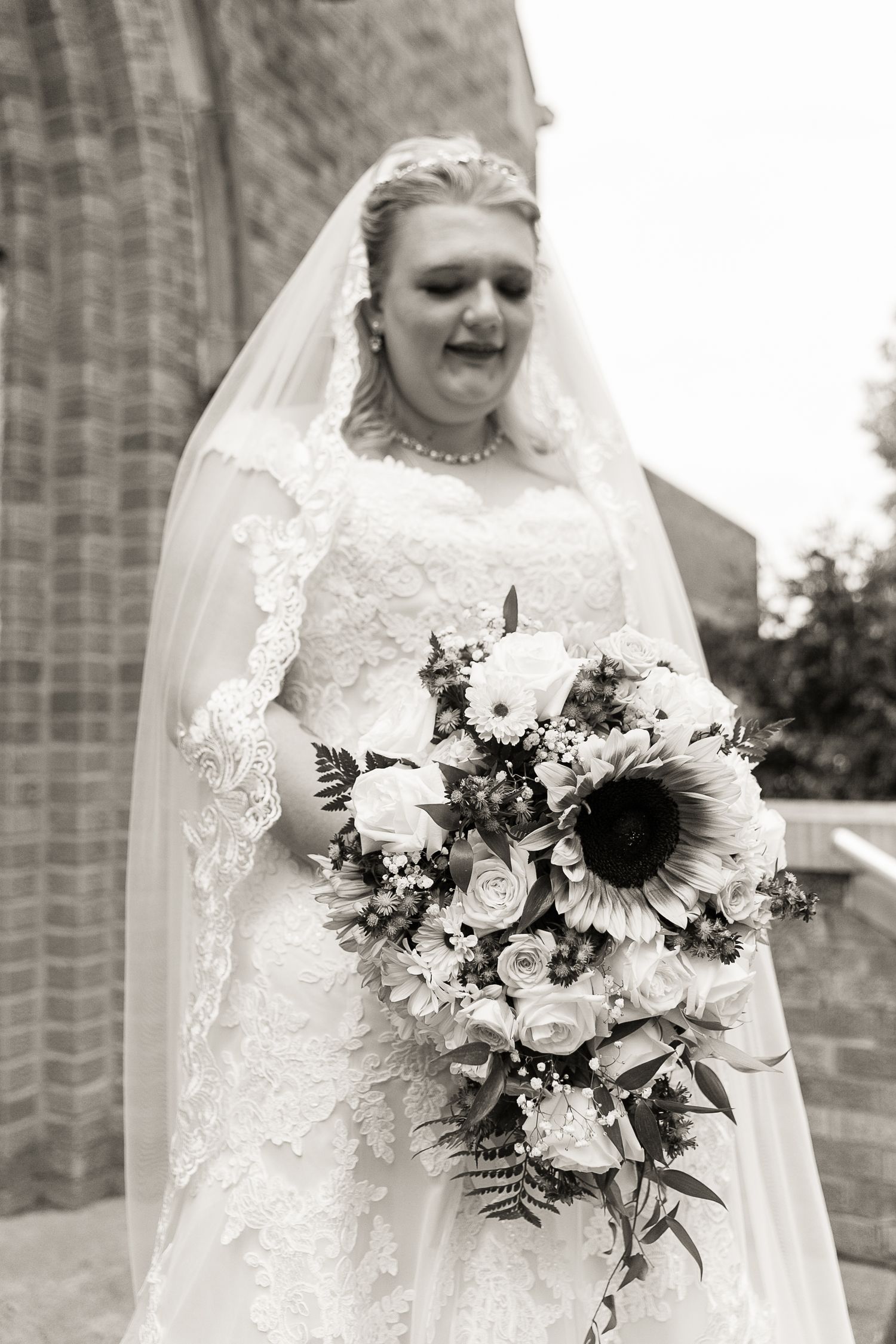Wedding bouquet featuring sunflowers and white roses with lace gown details.