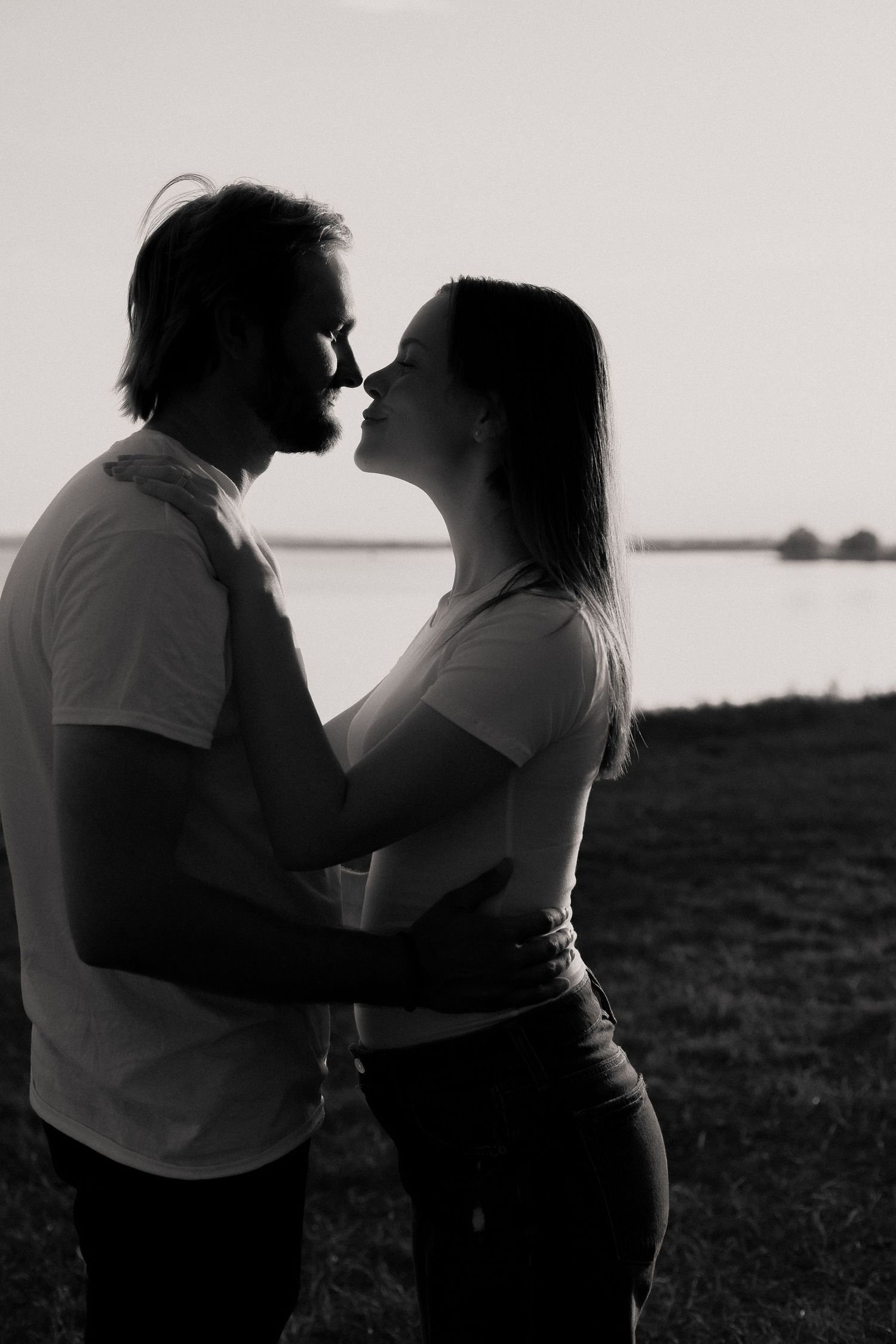 Silhouette of romantic couple about to kiss at sunset by water.