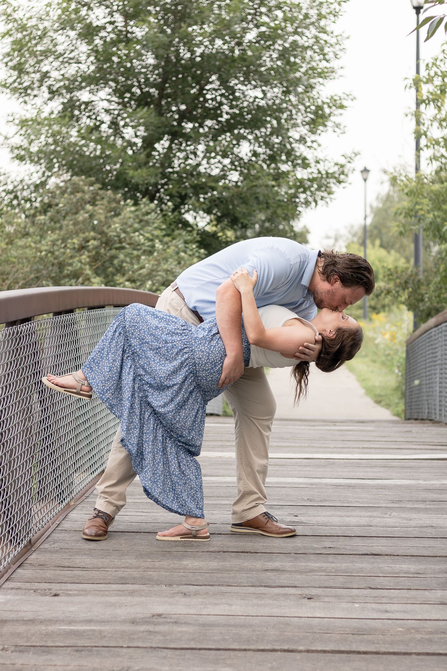 Couple sharing romantic dip pose on wooden bridge during engagement photoshoot.