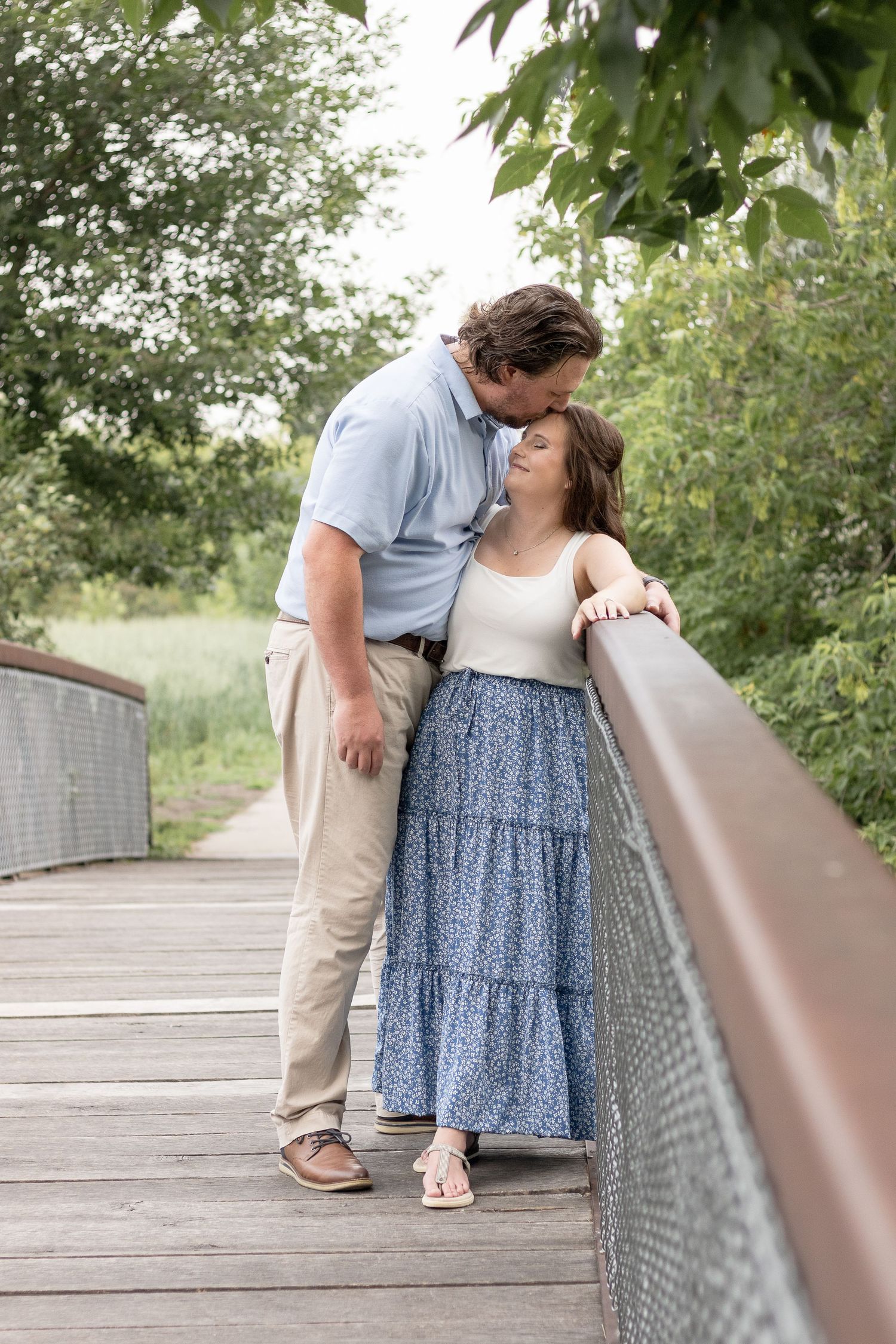 Sweet couple sharing an intimate moment on a wooden bridge surrounded by lush greenery.