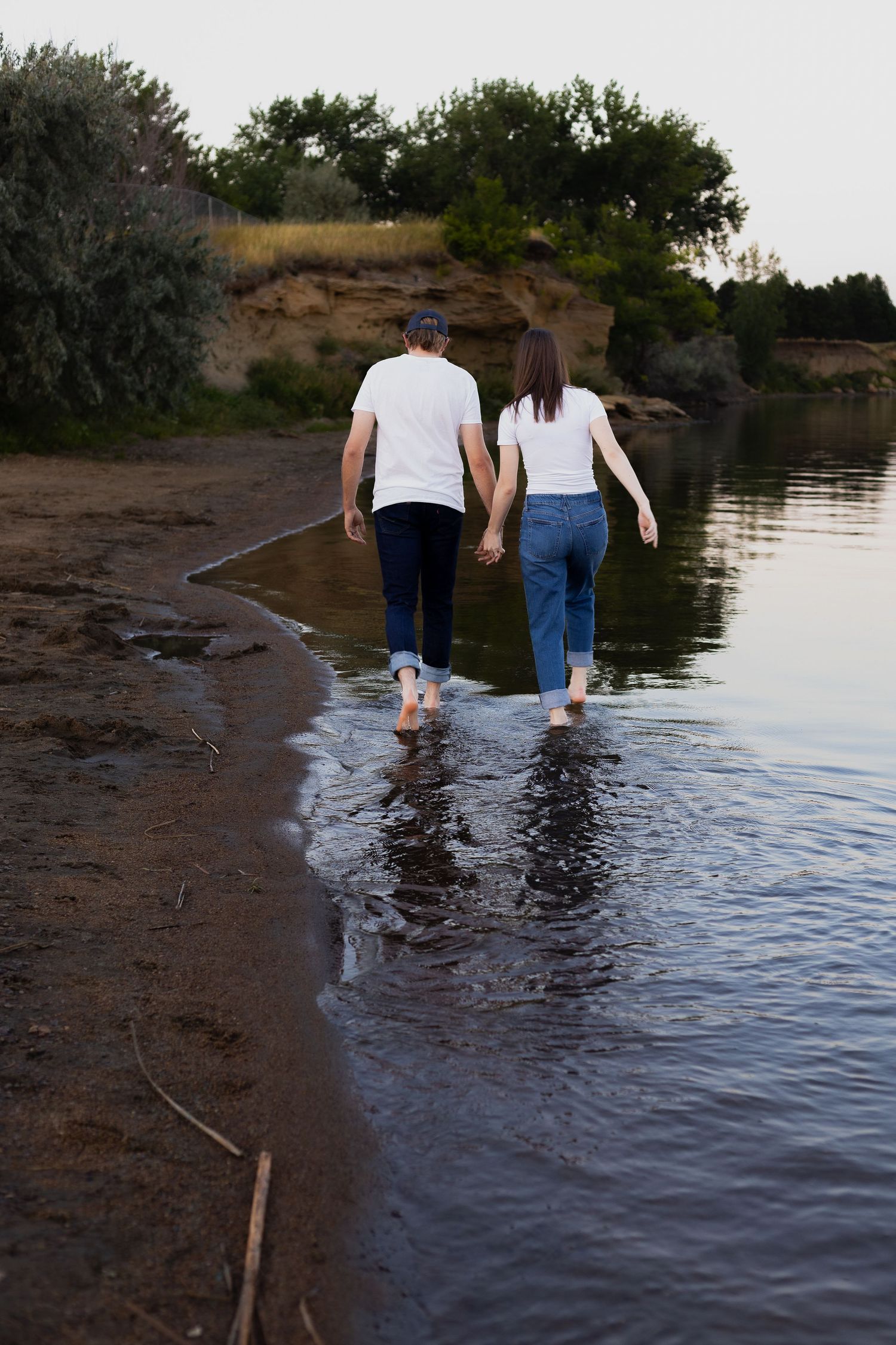 Couple walking barefoot along shoreline holding hands.