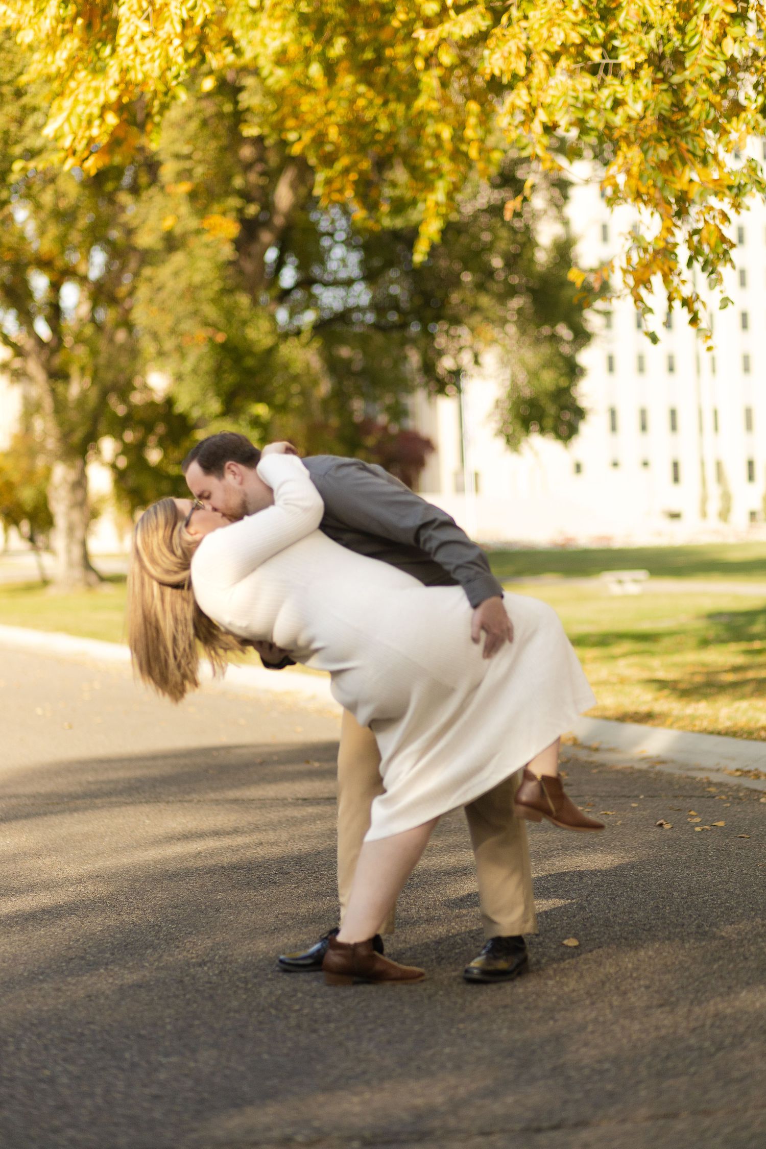 A romantic dip pose of a couple on a path with golden autumn trees in the background.