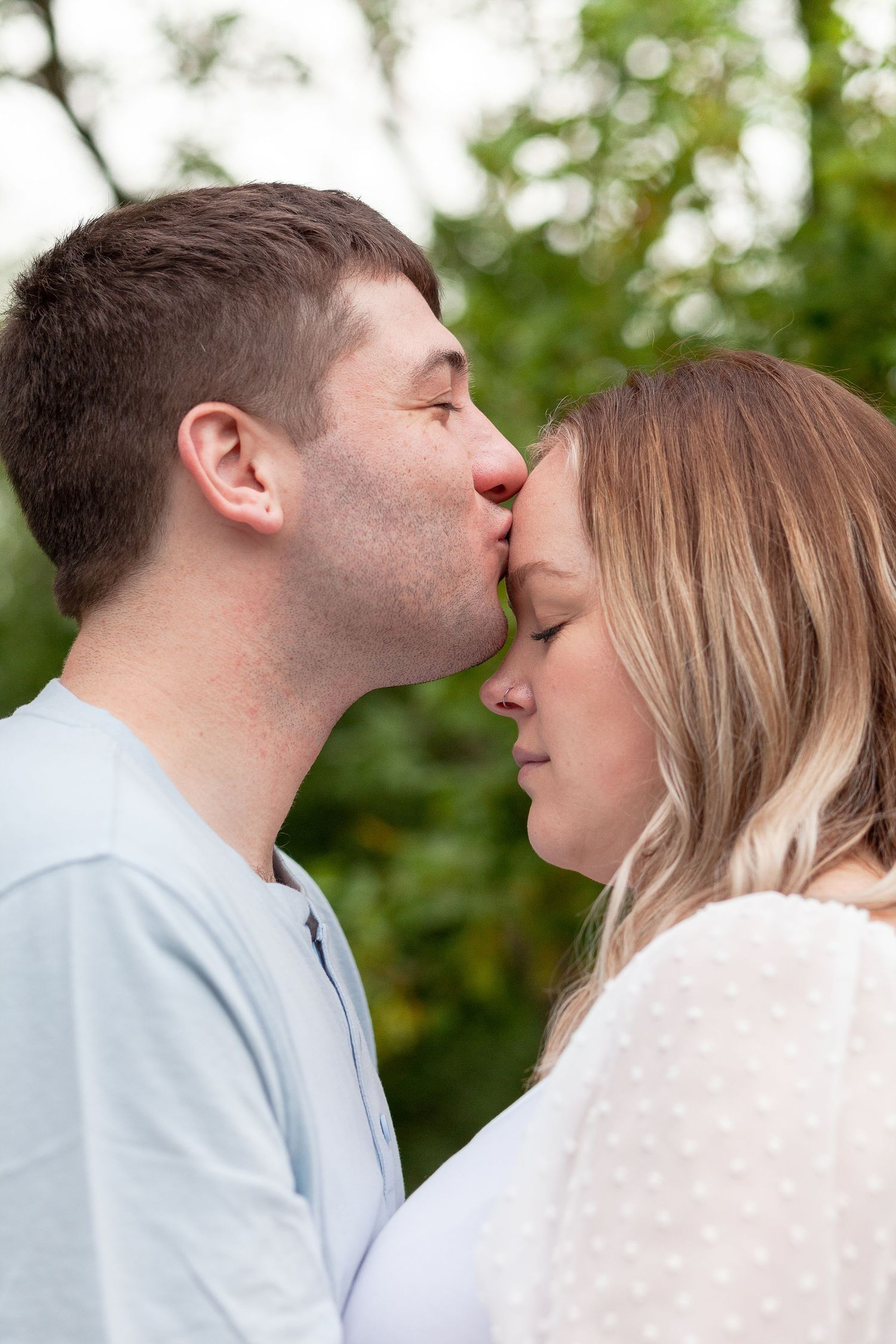 Close-up of a tender forehead kiss between a romantic couple in an outdoor setting with bokeh background.