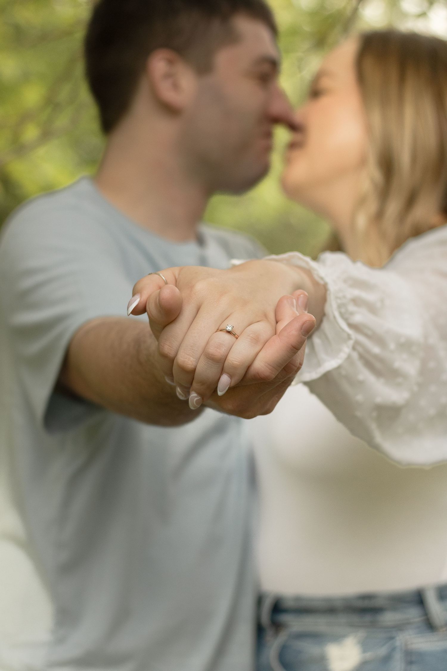 Close-up of engaged couple's hands with ring while sharing an intimate moment outdoors.