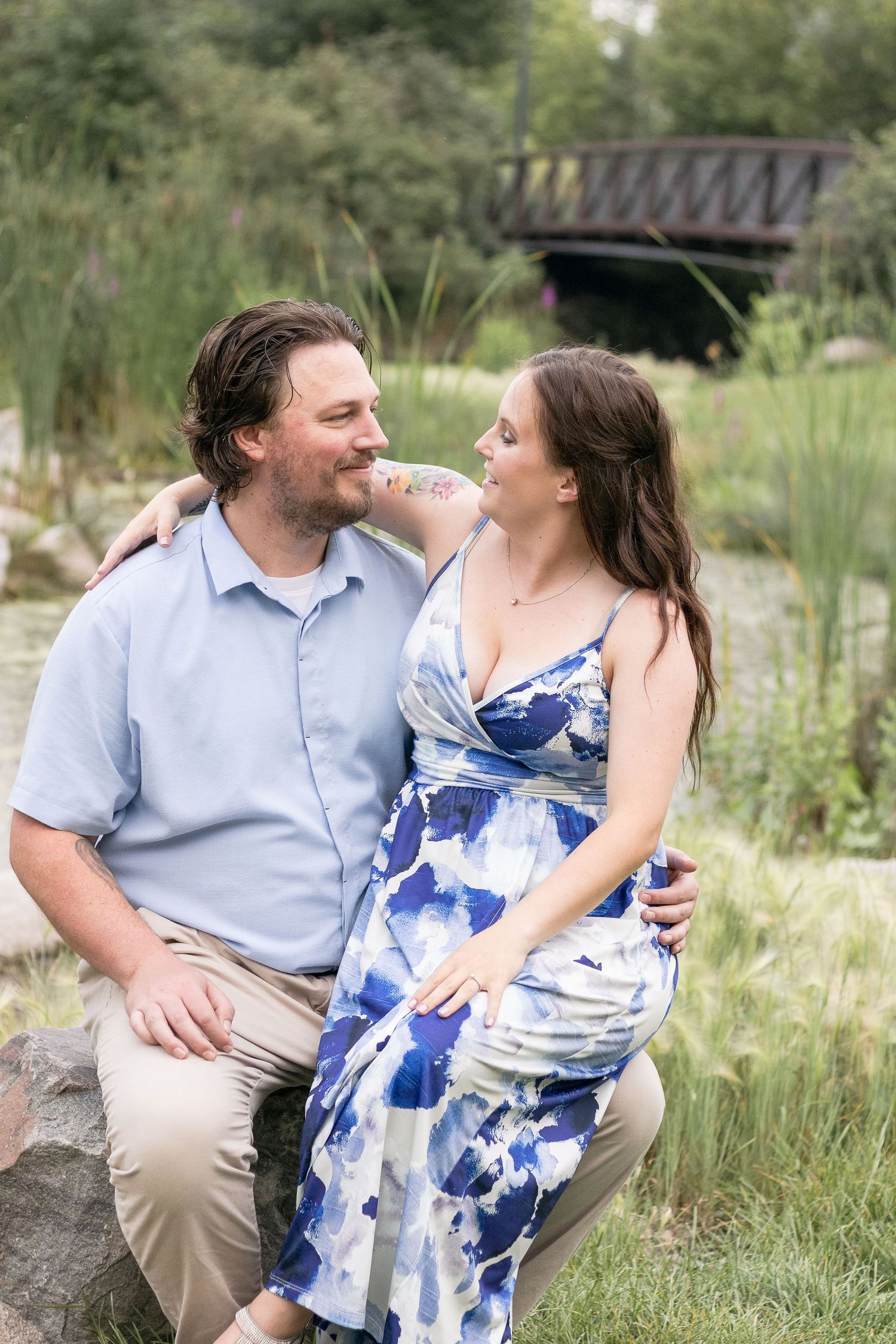 A couple sits on rocks near a pond, sharing an intimate moment in a natural setting.