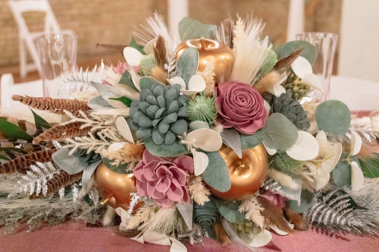 An elegant centerpiece with dusty rose flowers, gold accents, and eucalyptus on a wedding table.