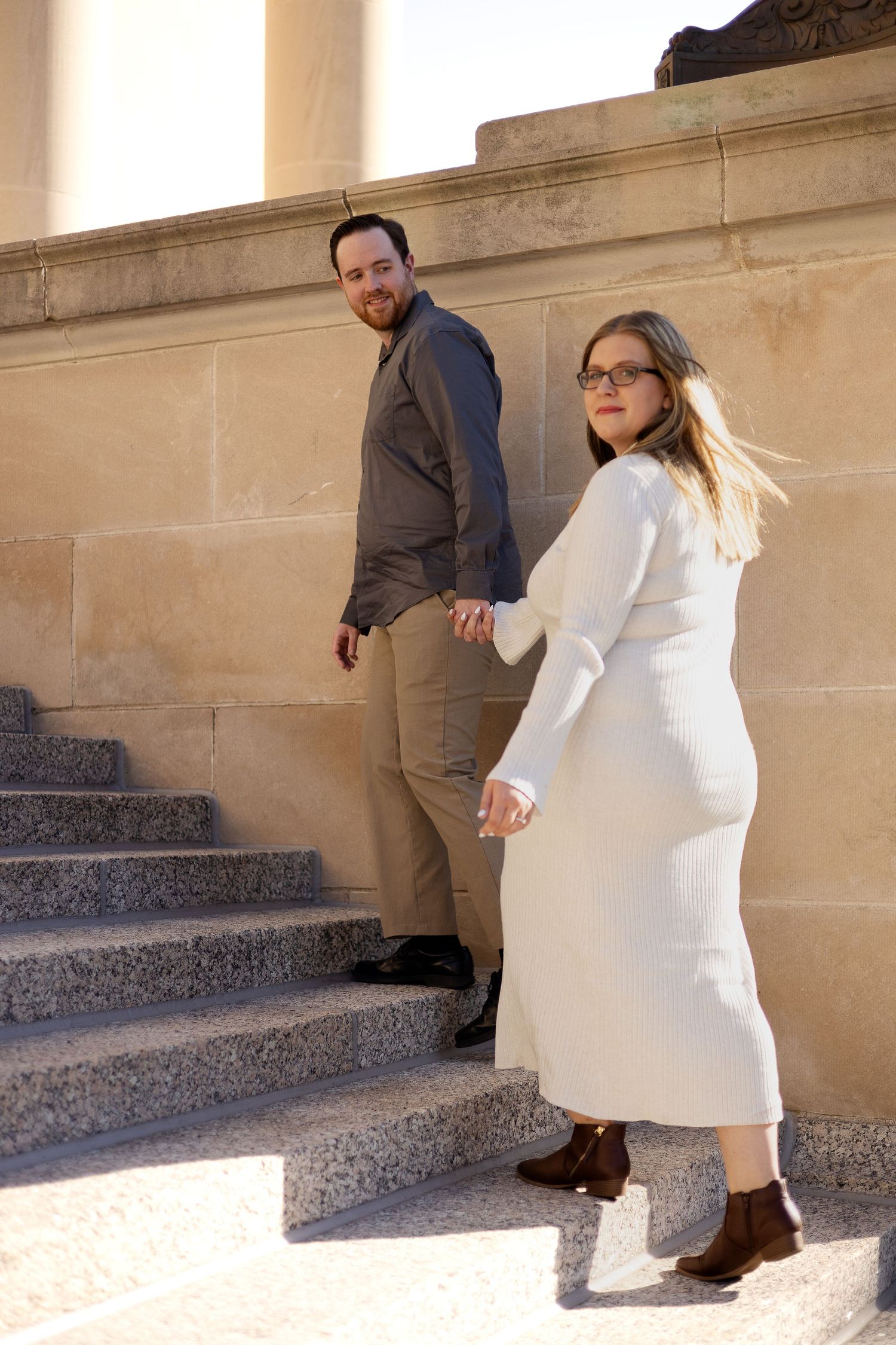 A couple posing together on stone steps in formal attire.
