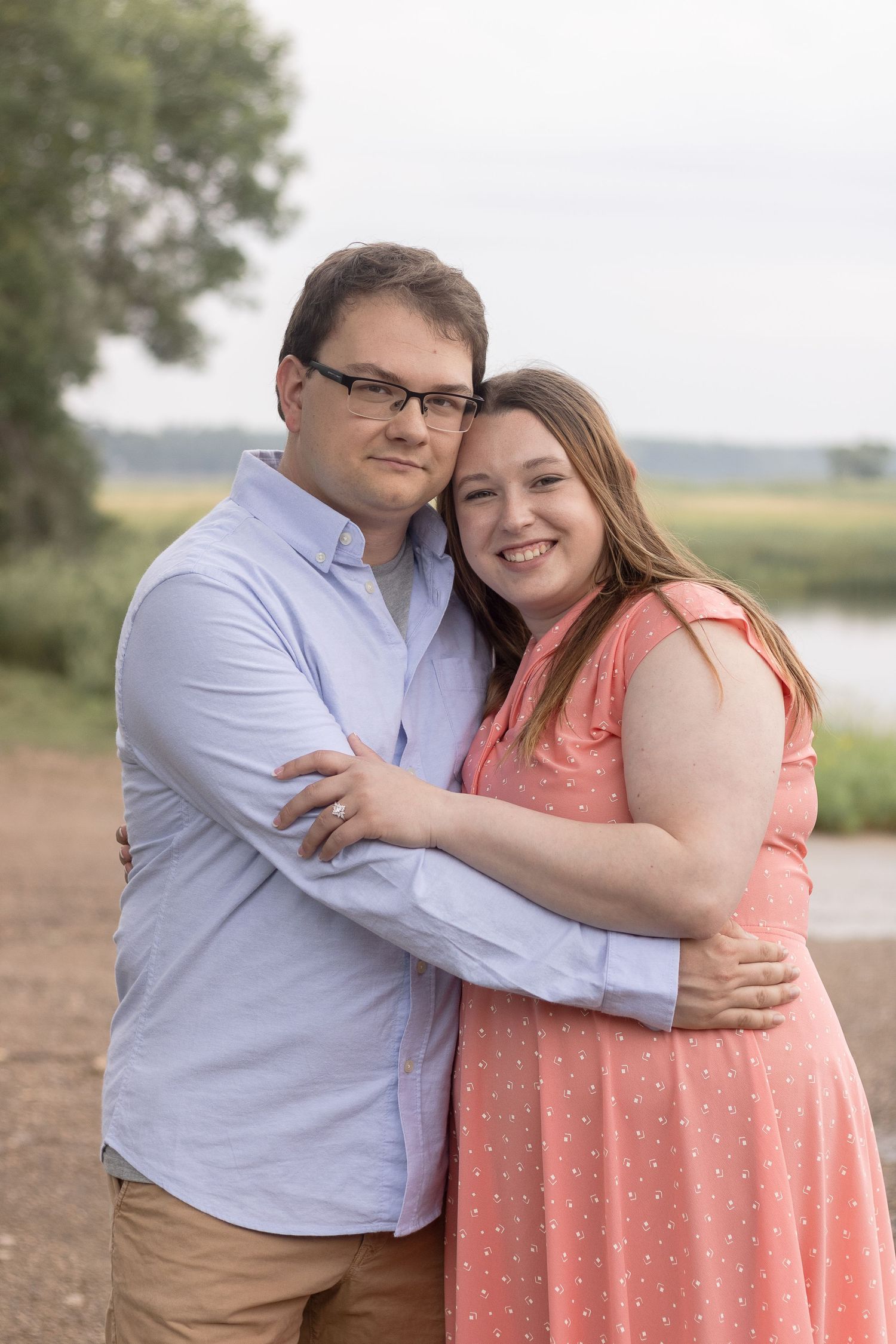 A loving couple shares a tender embrace outdoors by a waterfront on a sunny day.