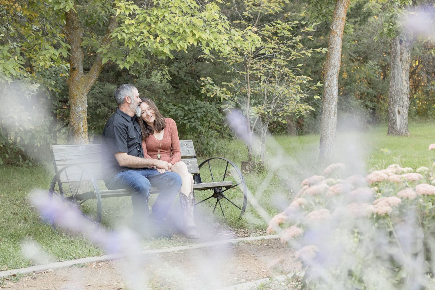 A romantic moment shared on a park bench surrounded by soft purple flowers.