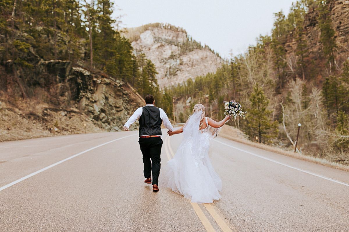 Couple walking down mountain road together in romantic wedding attire.