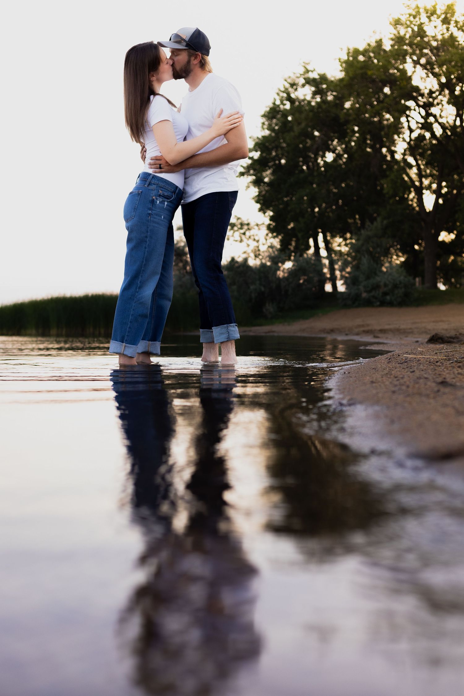 Couple standing in ankle-deep water with reflection during sunset.