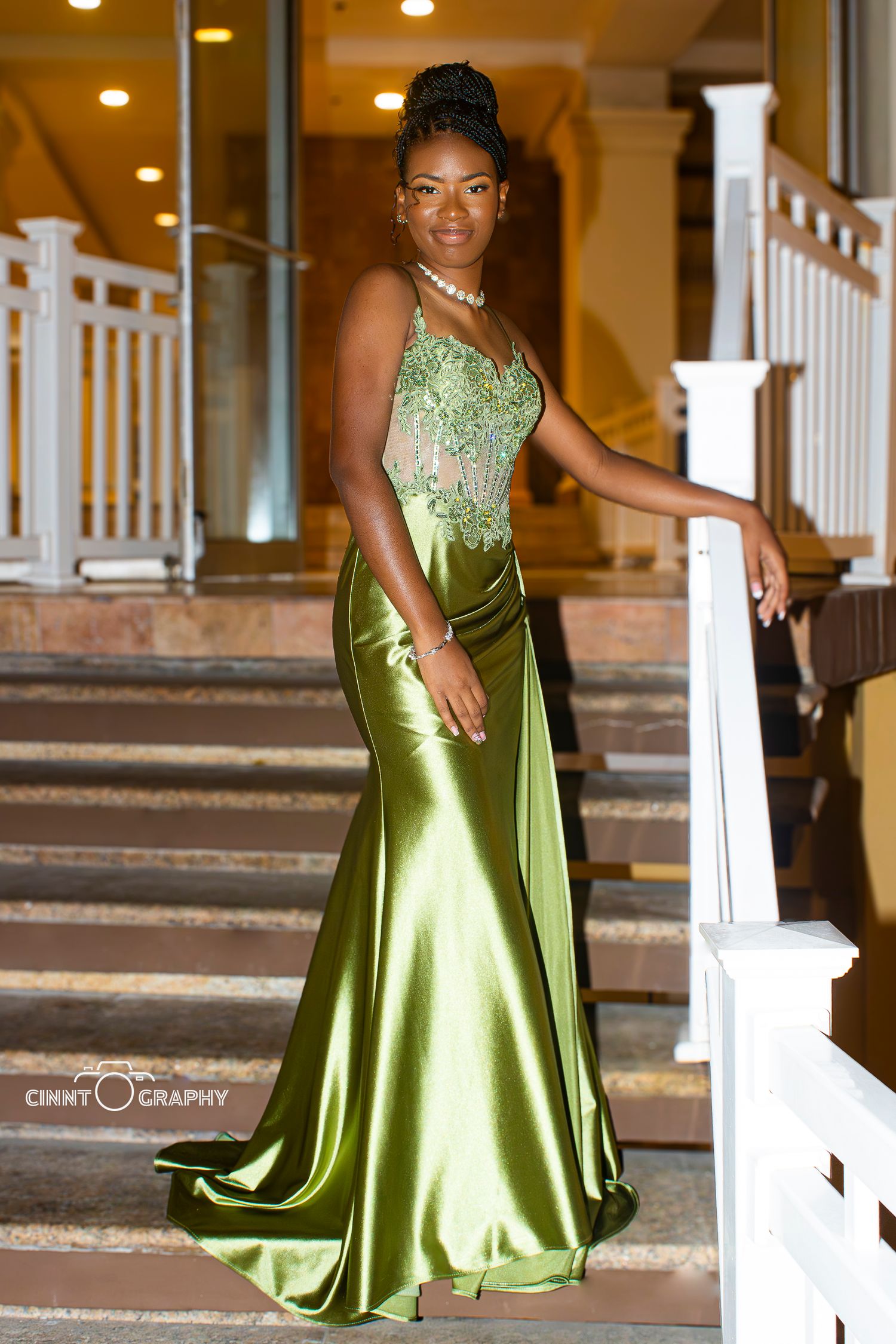 Elegant prom photo of someone wearing a shimmering lime green satin gown with lace details on a staircase.