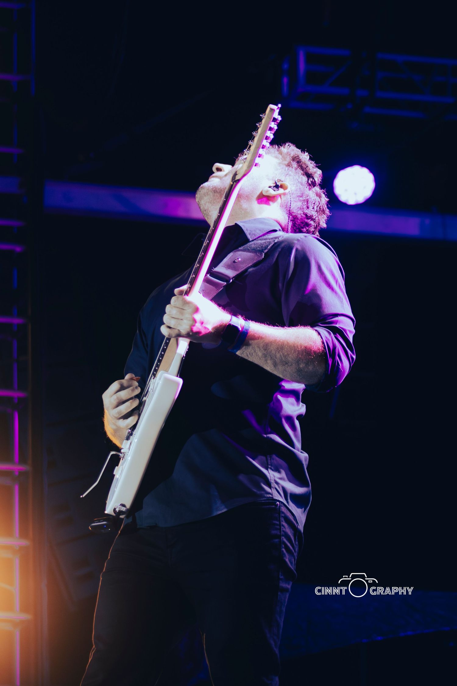 Guitarist passionately performs on stage illuminated by blue and purple concert lighting.