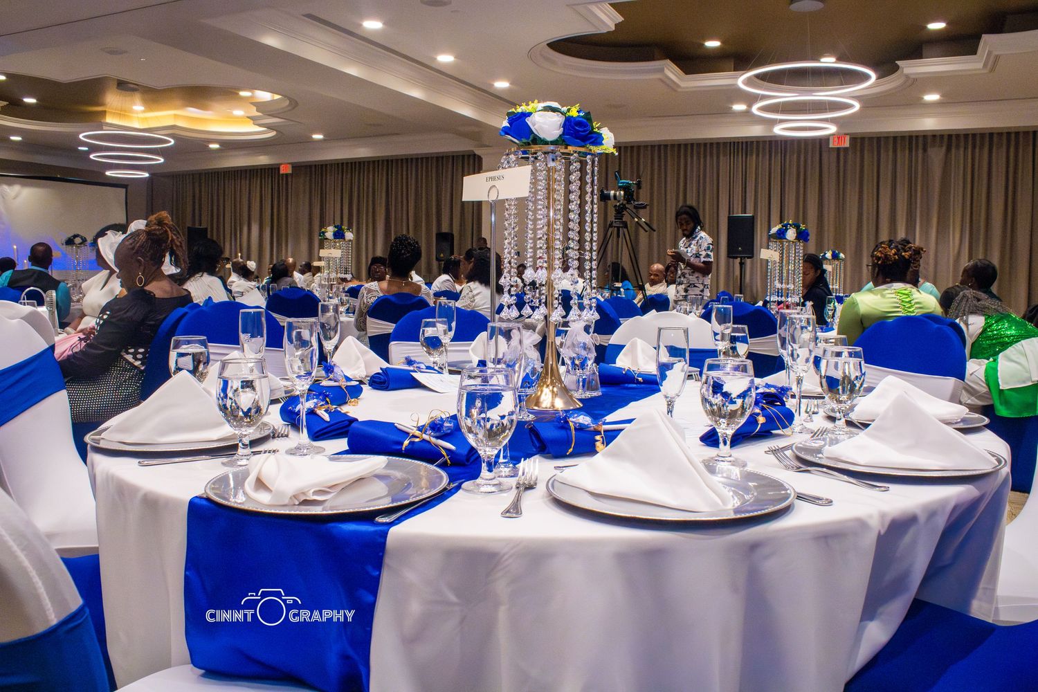 Event tables decorated with royal blue and white linens featuring elegant place settings in a modern banquet room.