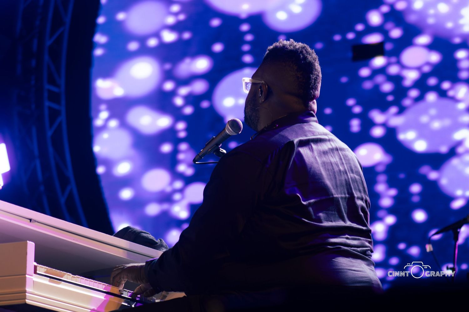 Musician performs at piano against backdrop of glowing blue bokeh lights during stage performance.