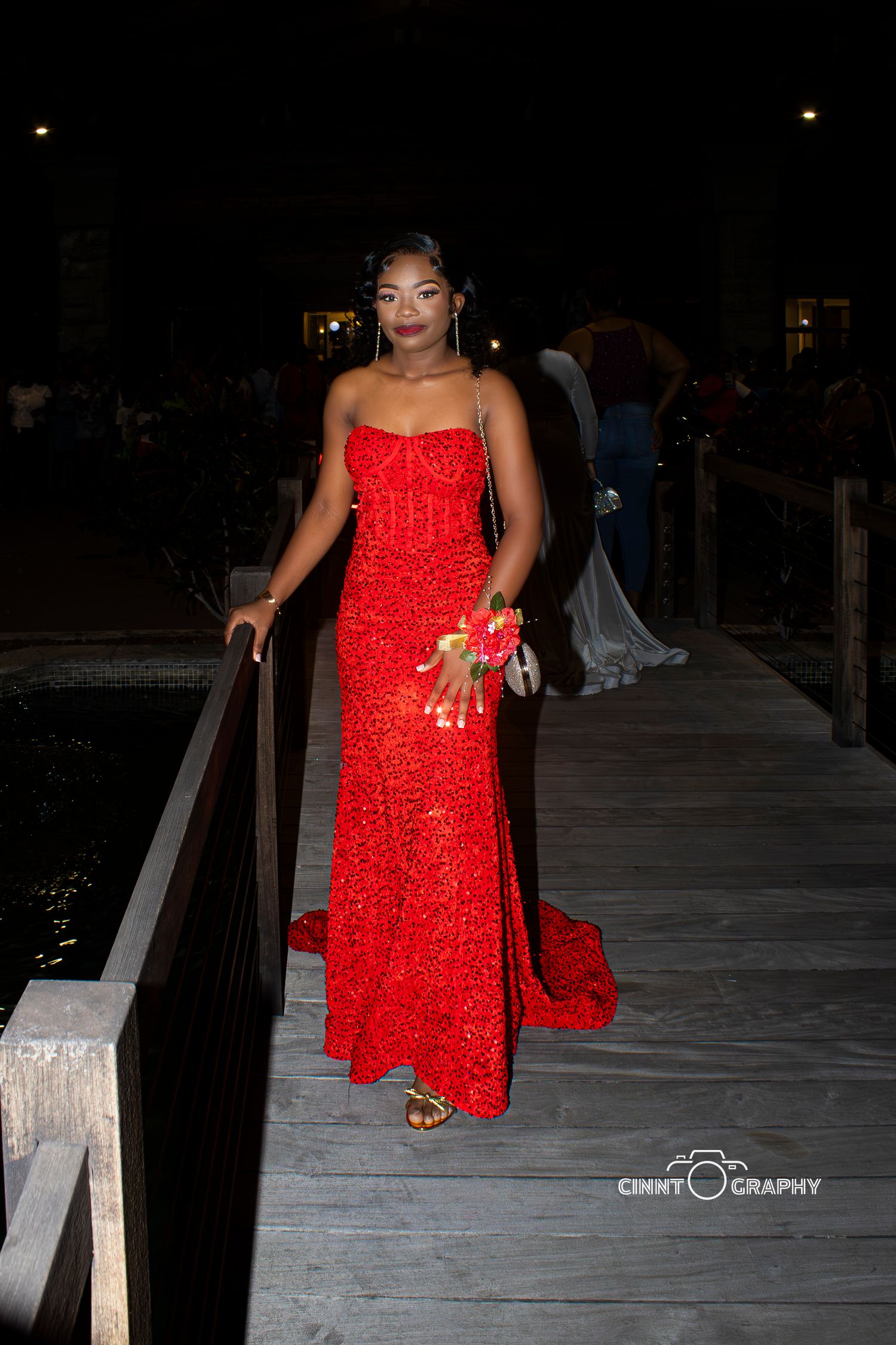 Person in a vibrant red dress poses on a wooden boardwalk at night with creative lighting and composition.