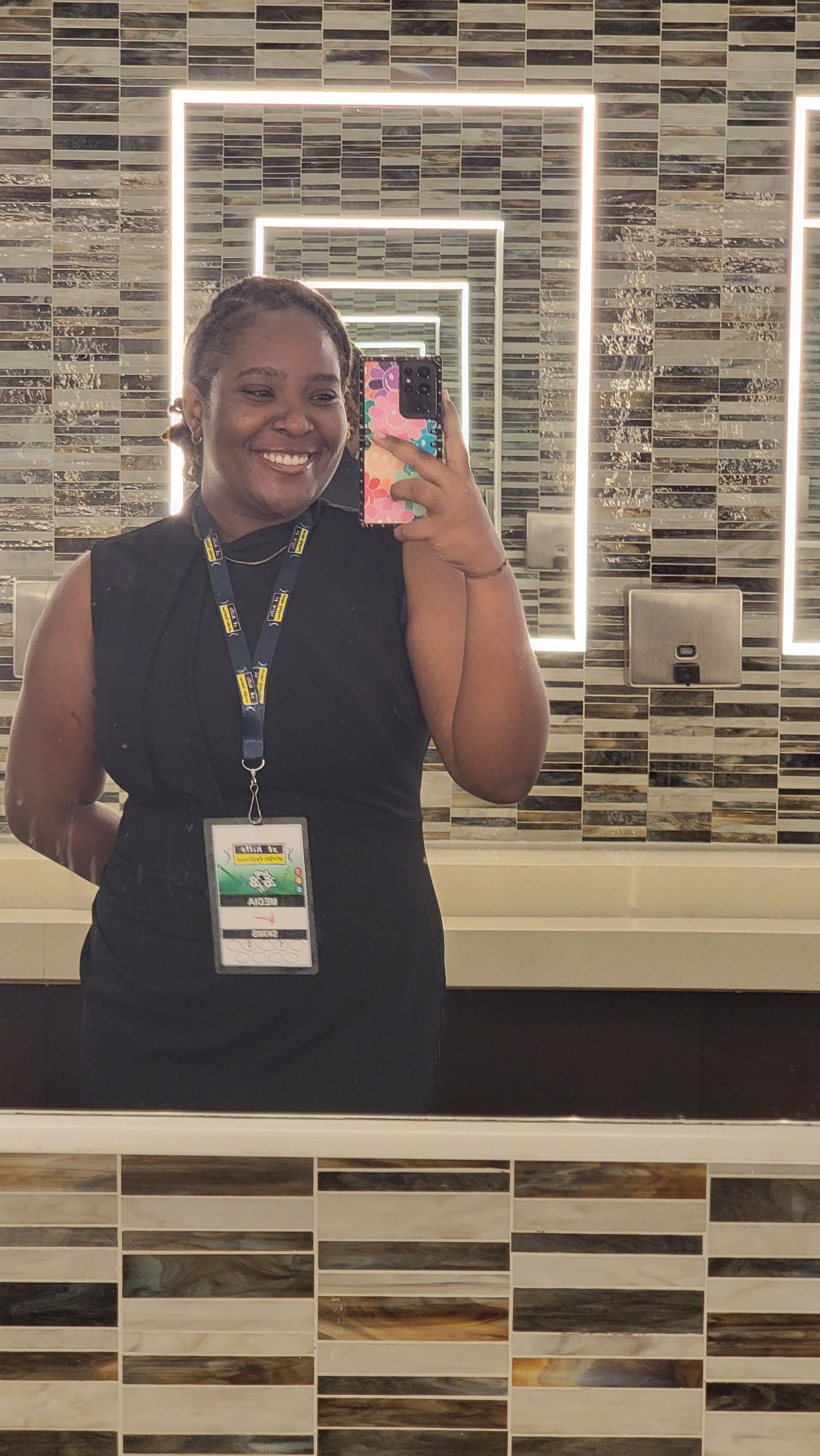 A mirror selfie taken in a modern bathroom with geometric tiled walls and LED-illuminated mirrors creating an infinity effect.