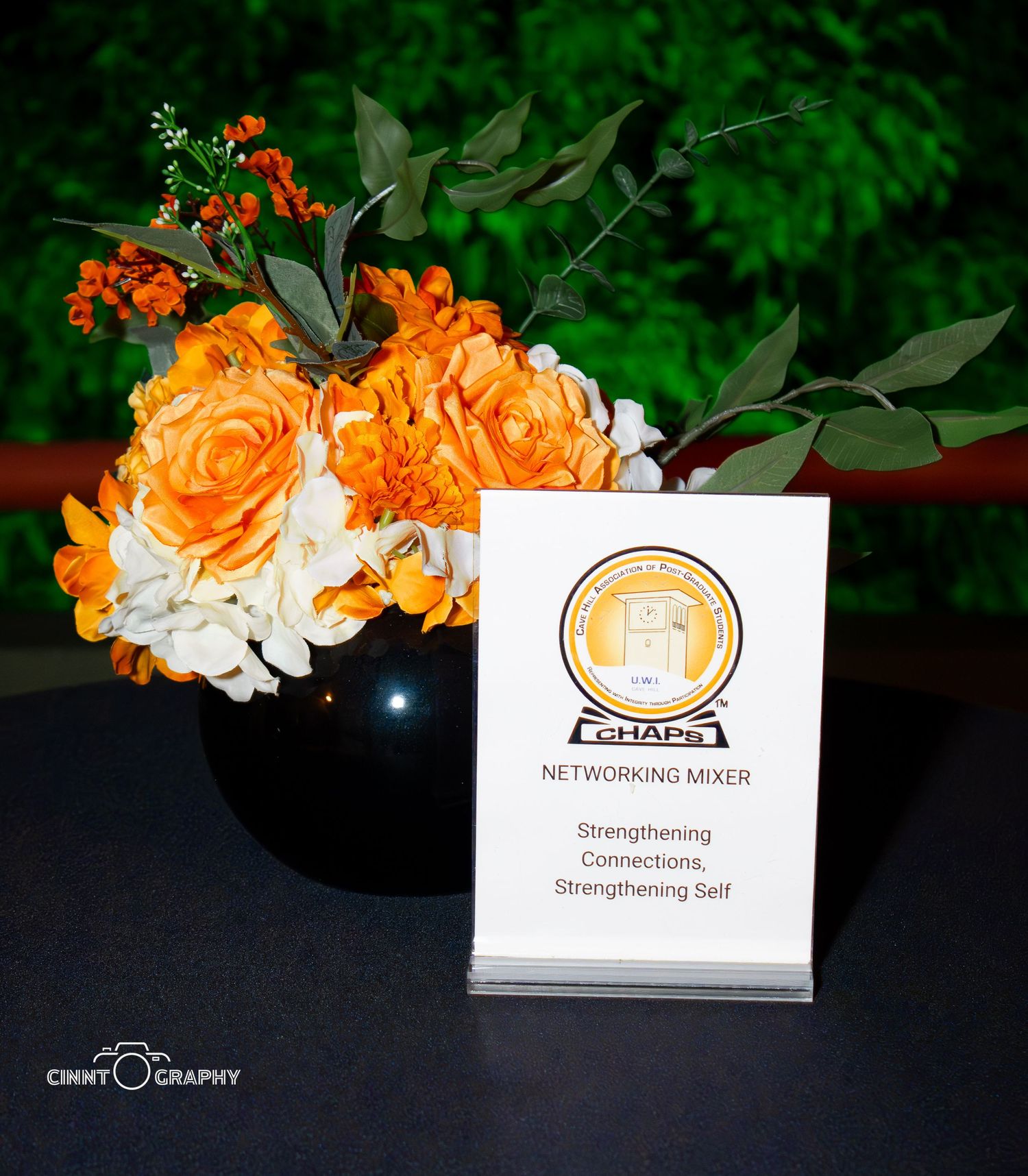Orange and white floral arrangements with business cards displayed against dark background at a networking event.