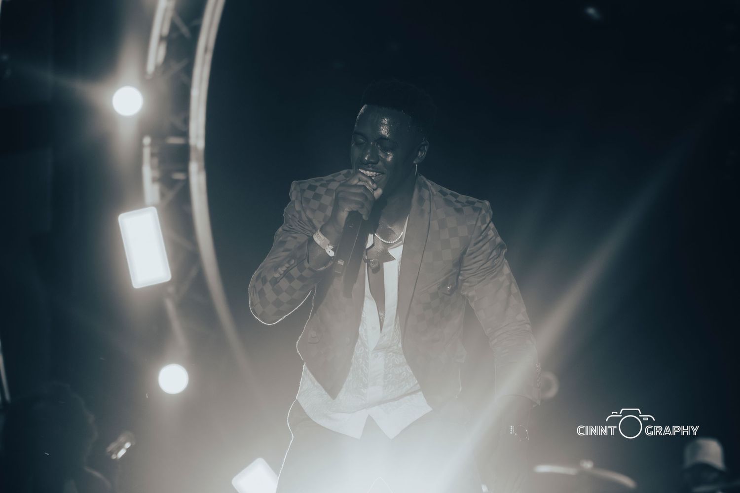 A performer in formal attire is captured in monochromatic tones under dramatic stage lighting.