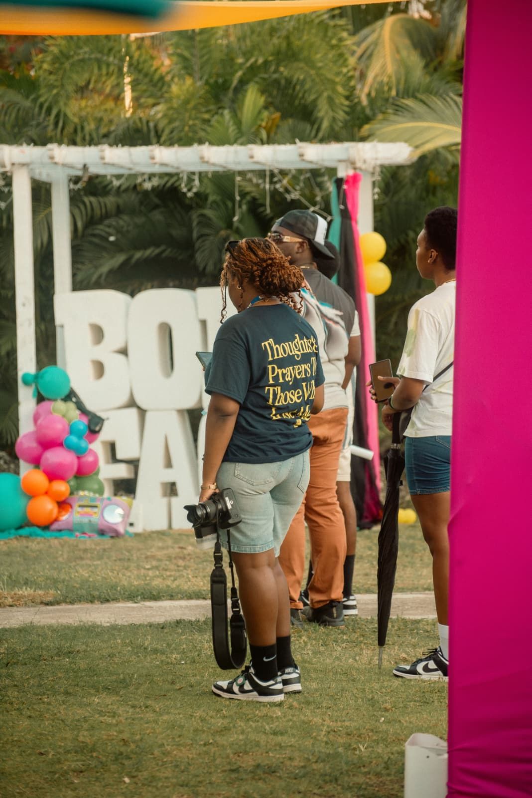 Multiple colorful balloons decorate an outdoor setting with a large white display sign visible in the background.