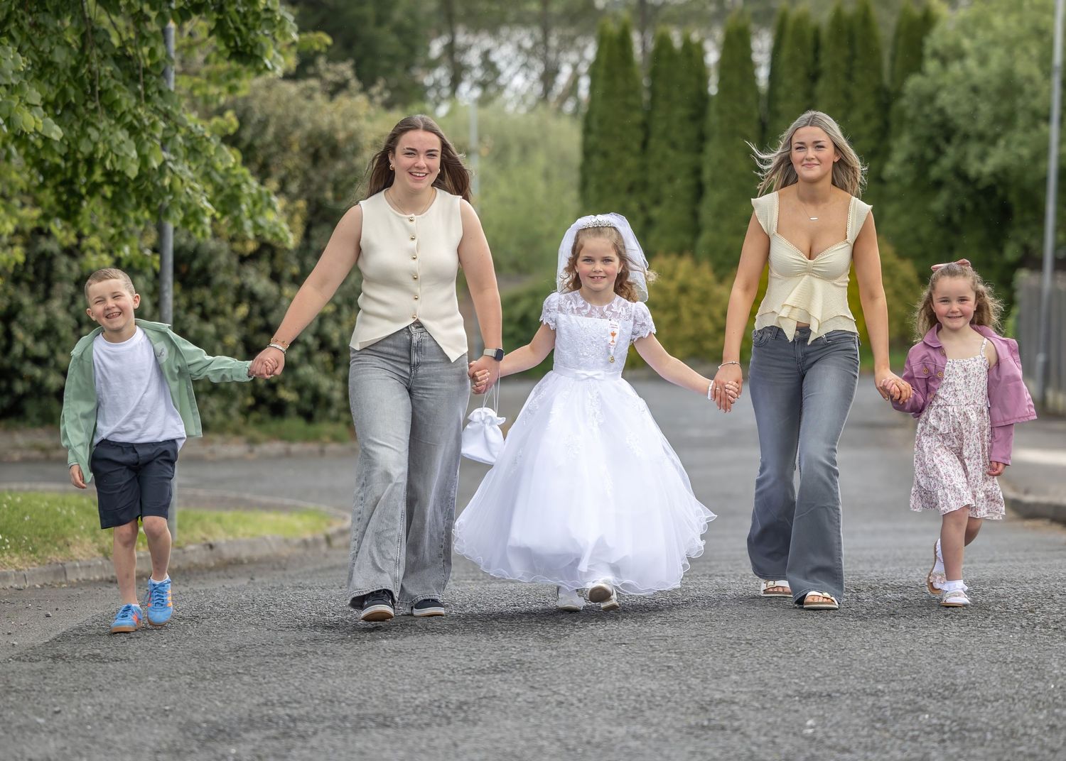 Five people walking hand-in-hand on a path, with a girl in a white communion dress in the center.