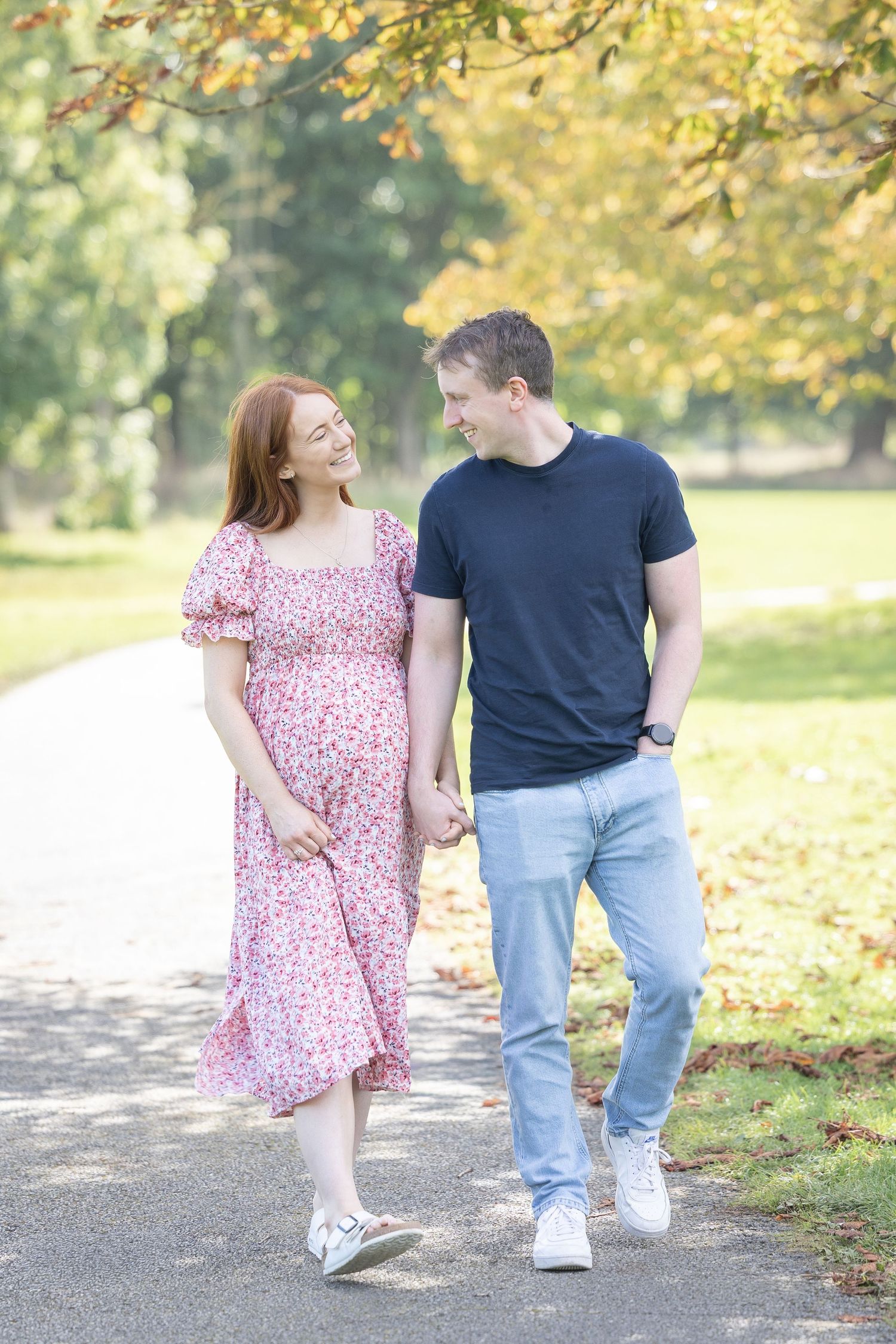 Couple walking and laughing together on autumn path with fallen leaves.
