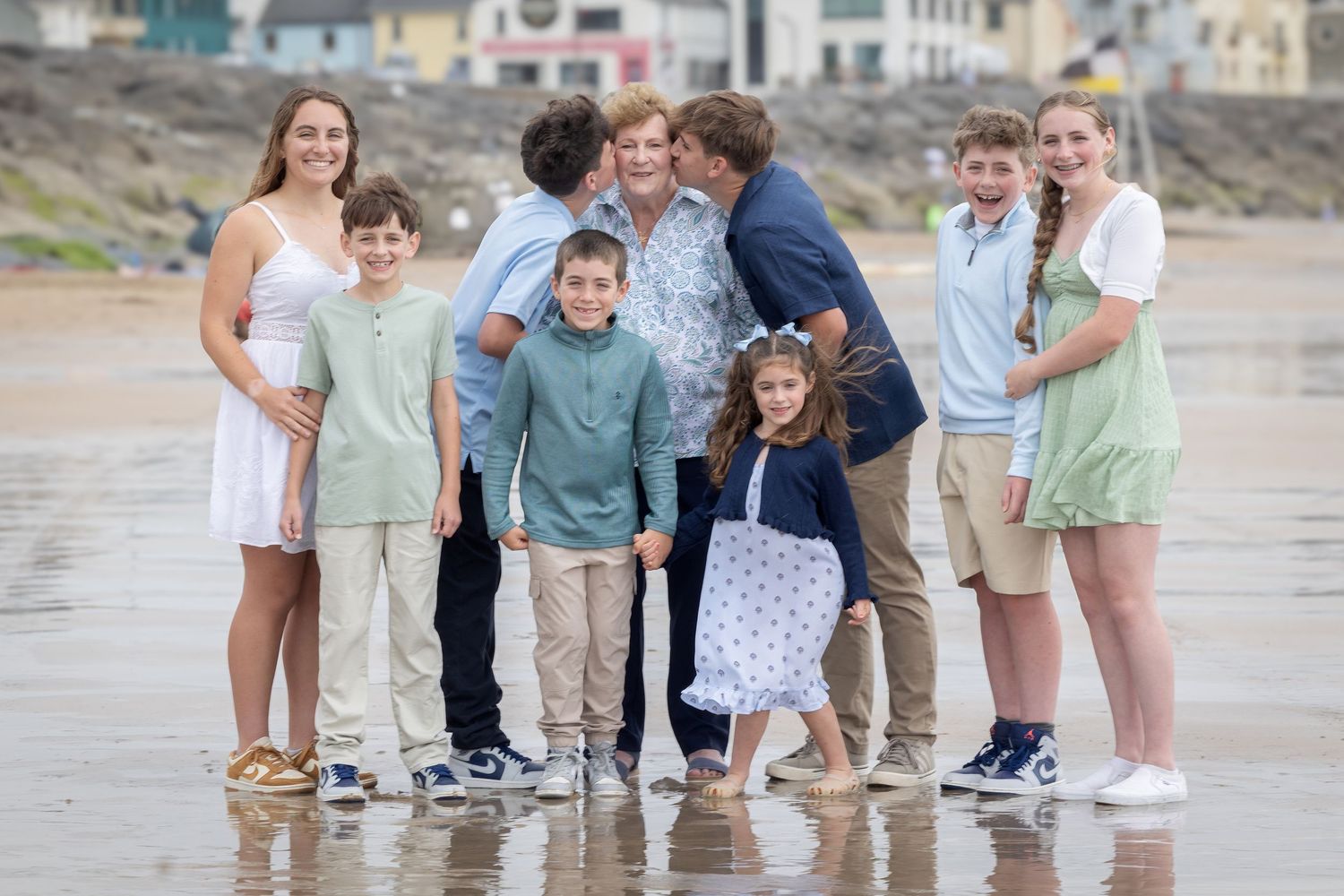 Large family group posing together on a sandy beach, smiling for a portrait on a cloudy day.