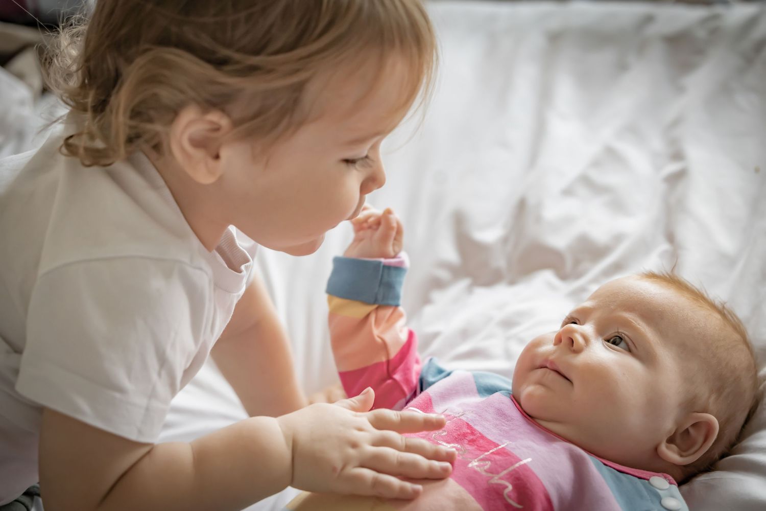 A tender moment between parent and child as they share laughter while lying on white bedding together.