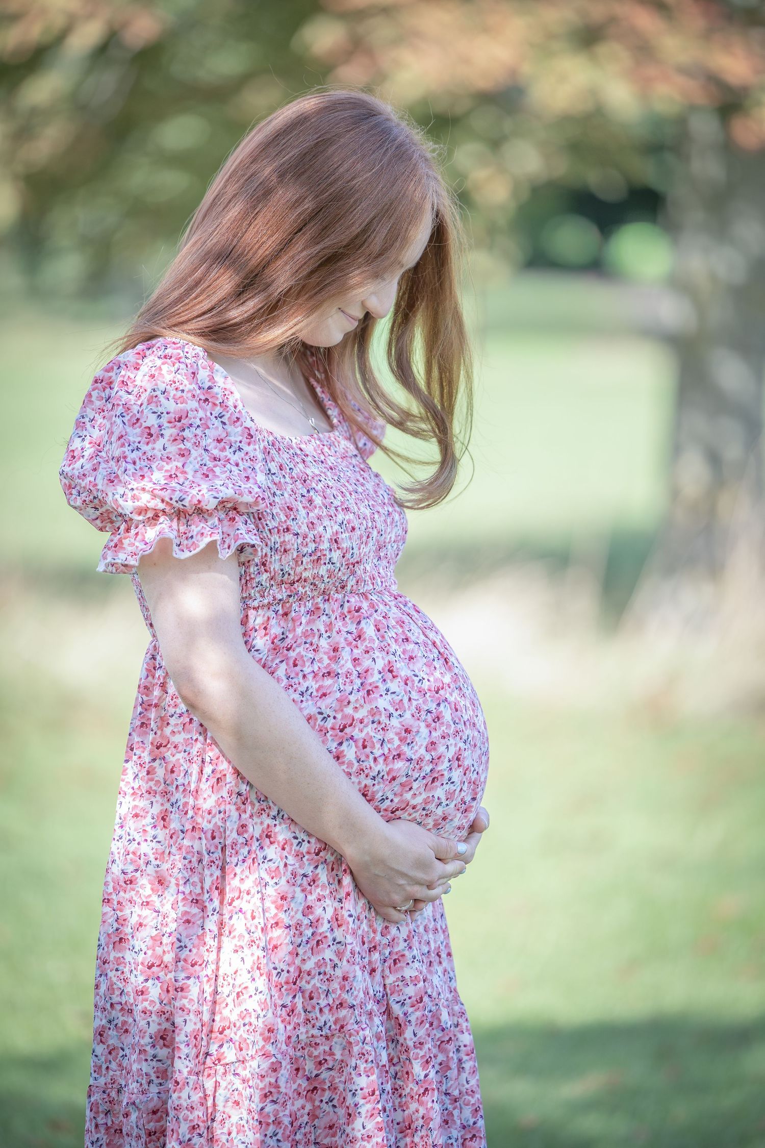 A person in a floral dress stands in a sunlit garden setting with soft bokeh background effect.