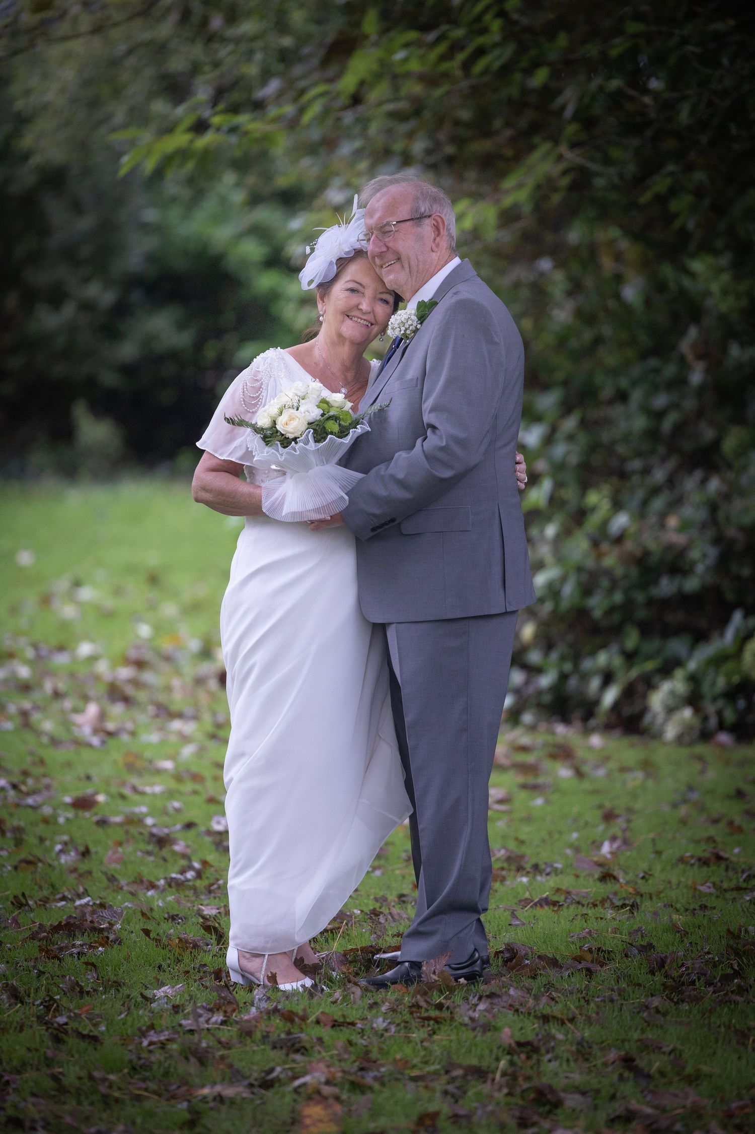 Couple embraces in garden setting wearing formal wedding attire.