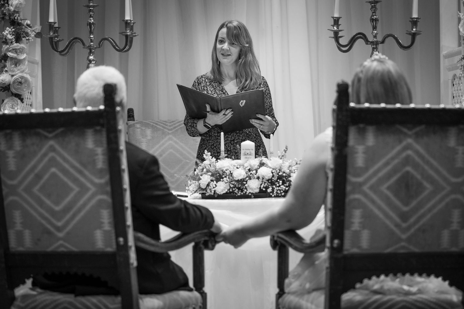 A black and white photograph shows a person reading at a formal dinner table with candelabras and elegant place settings.