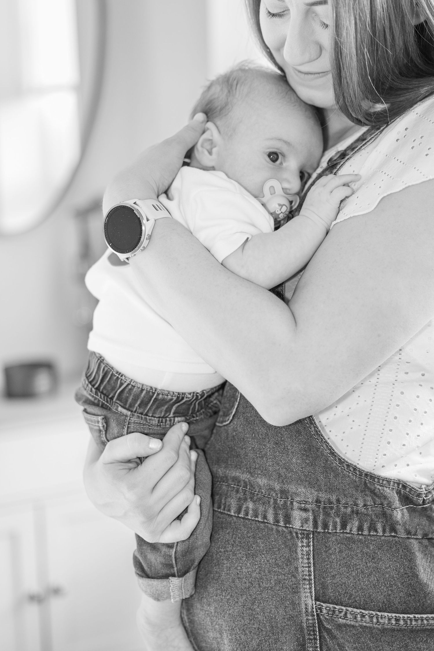 Baby rests peacefully against parent wearing denim in black and white portrait series.