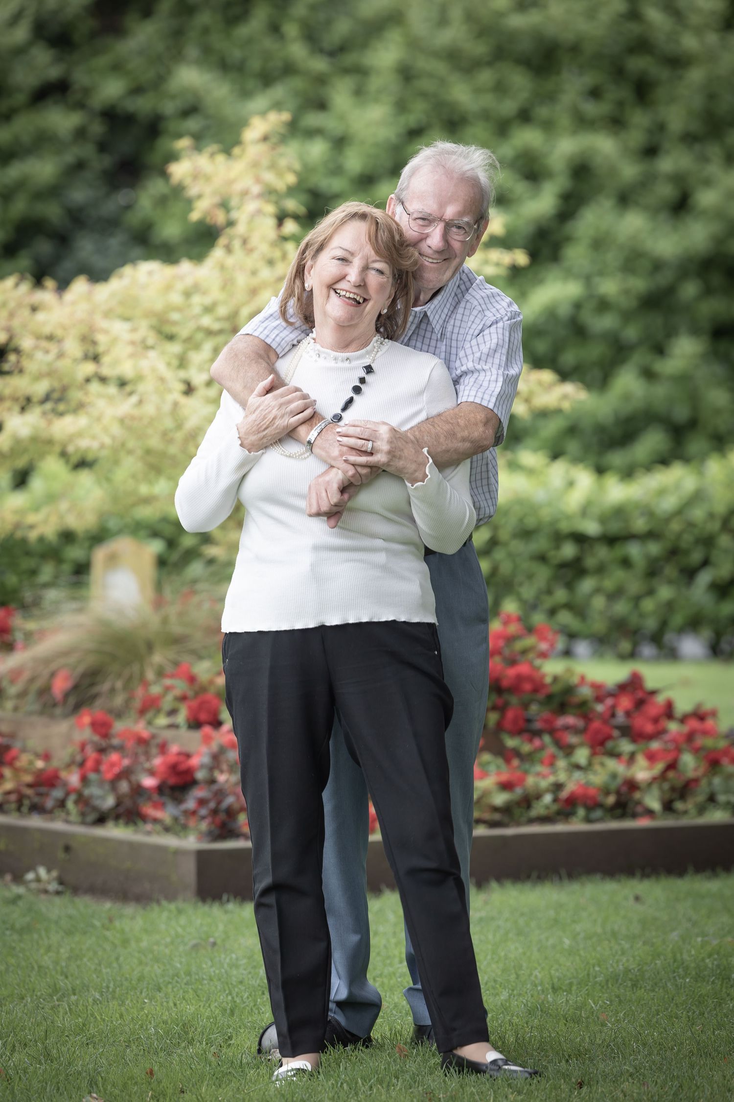 Couple embracing and laughing together in garden with red flowers.