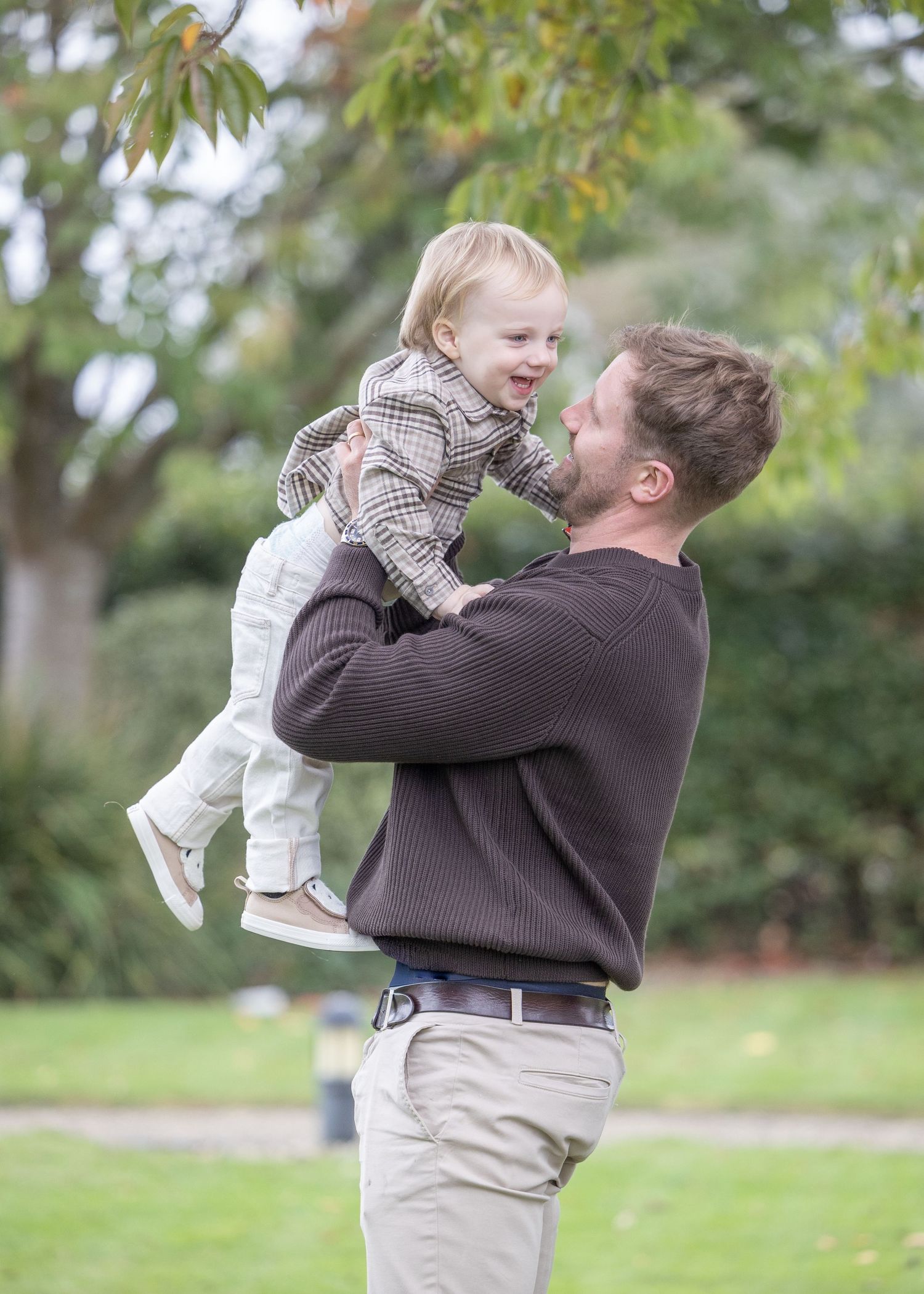 Playful sequence of parent lifting child in brown sweater outdoors.