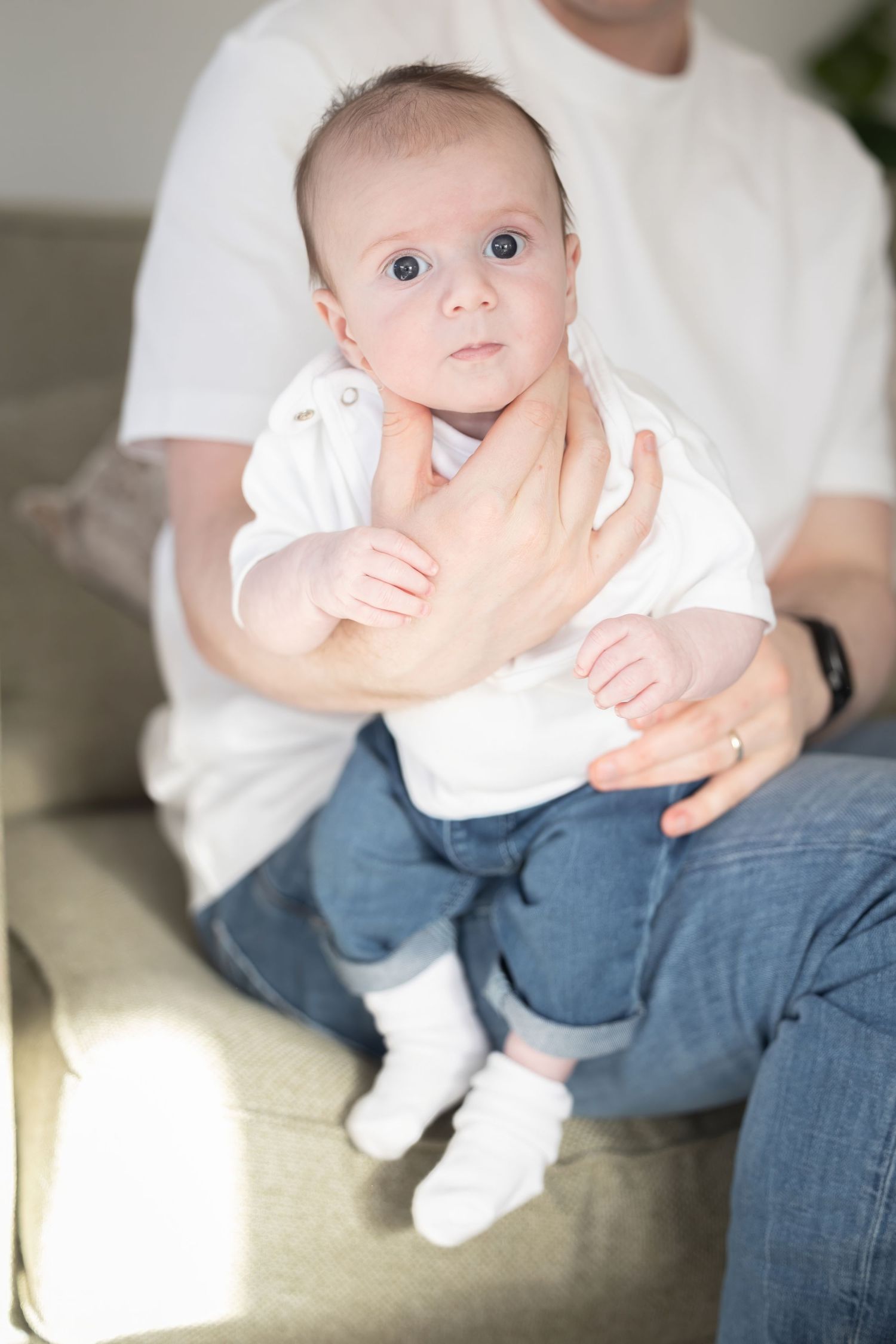 A series of photos showing a baby in white clothing sitting on someone's lap wearing blue jeans.