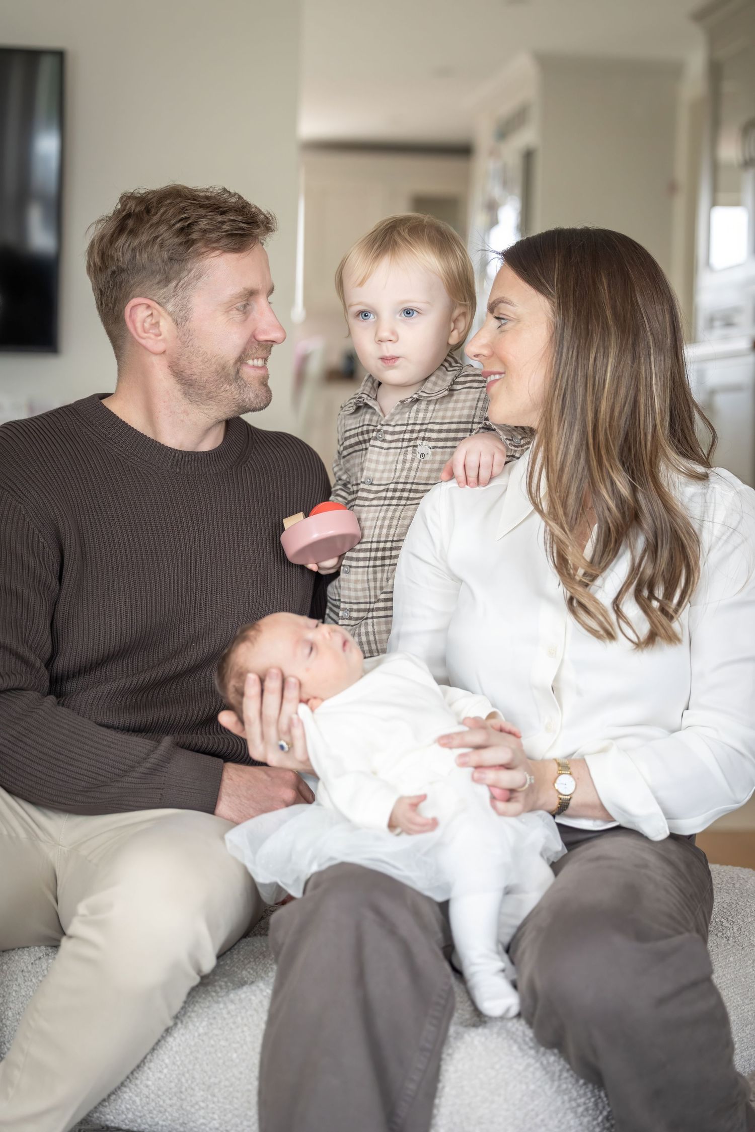 Family sitting together on a couch sharing tender moments with a newborn baby in a series of candid photos.