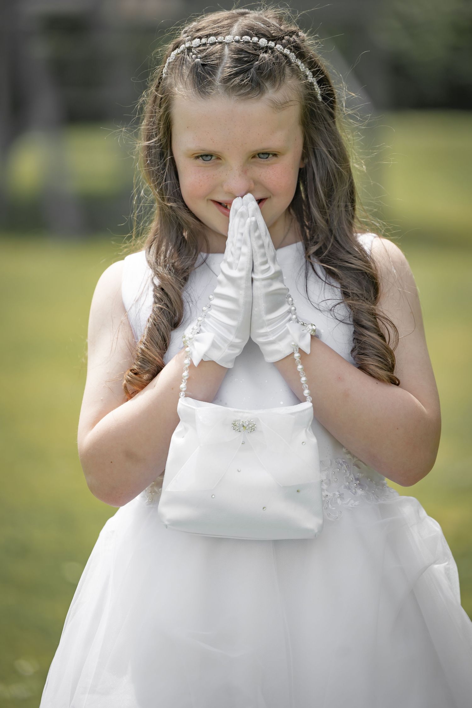 Child in white dress covering face with gloved hands in outdoor portrait series.
