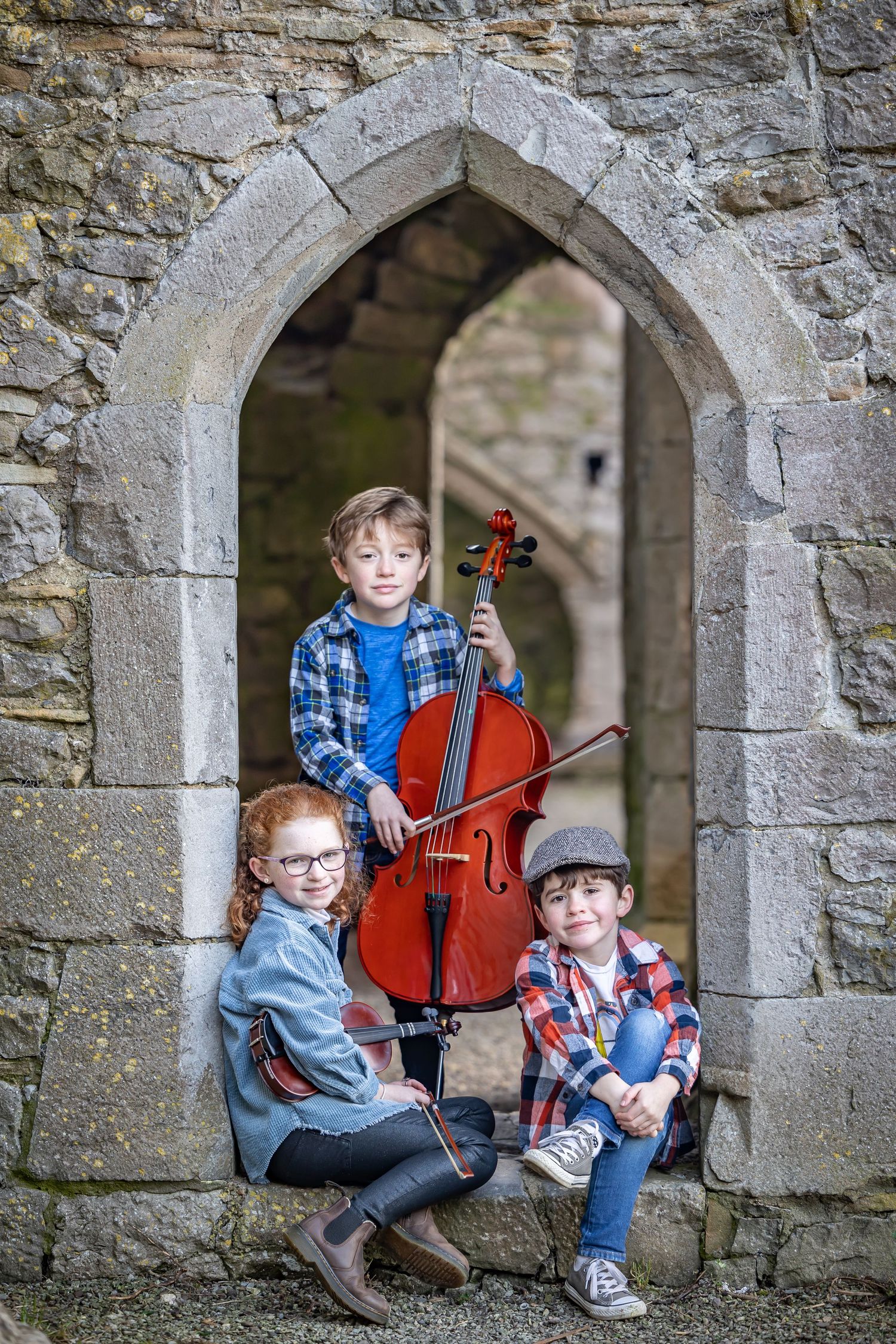 Stone archways in a historic castle wall frame musicians with instruments in a series of artistic photographs.