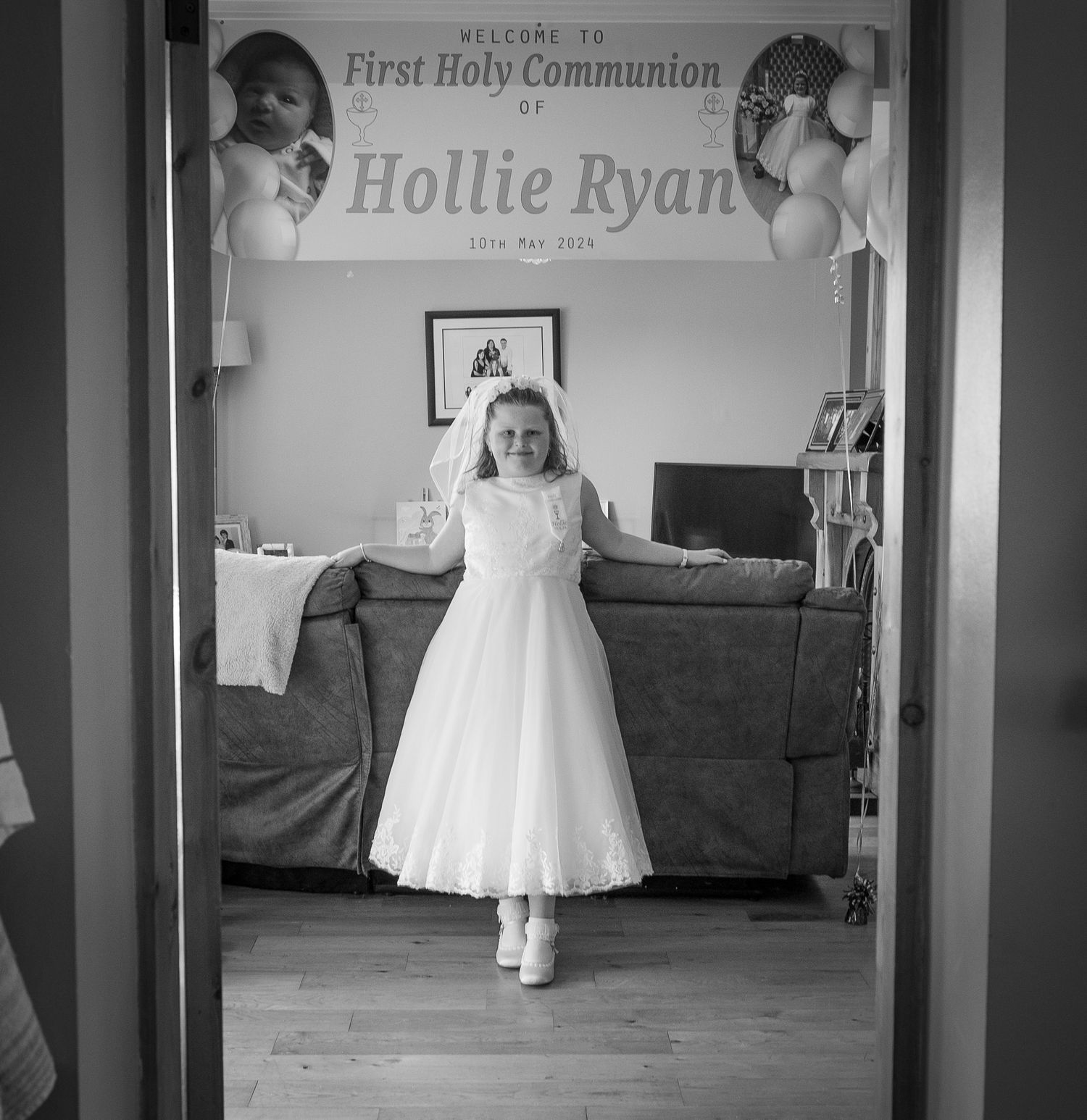 A series of black and white photos showing a child in a white communion dress standing in different poses at home.