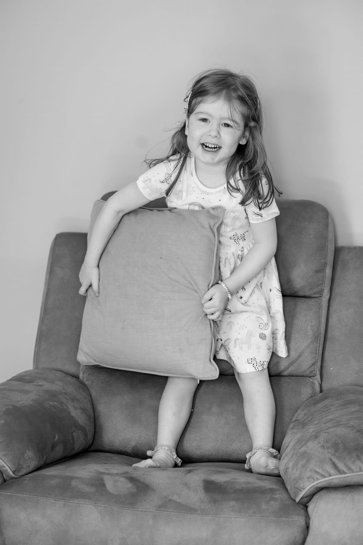 A sequence of black and white photos showing a child's playful movements and expressions while sitting on a gray couch.