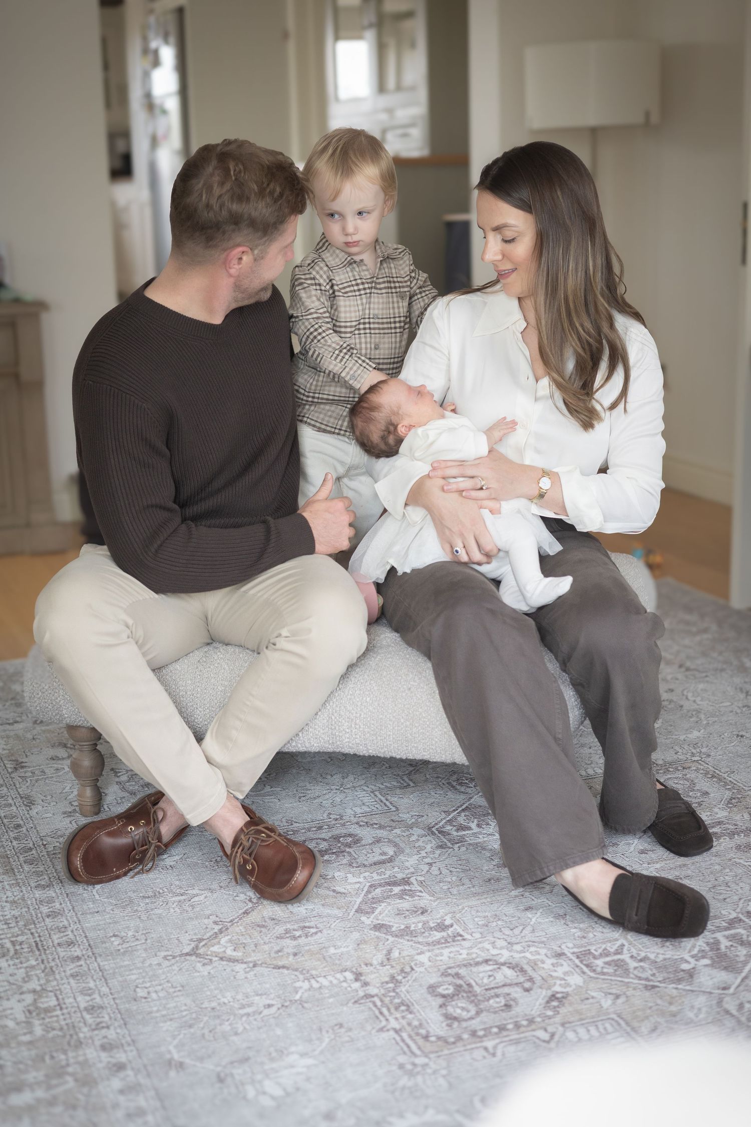Family members relaxing together on a gray patterned rug in a bright room.