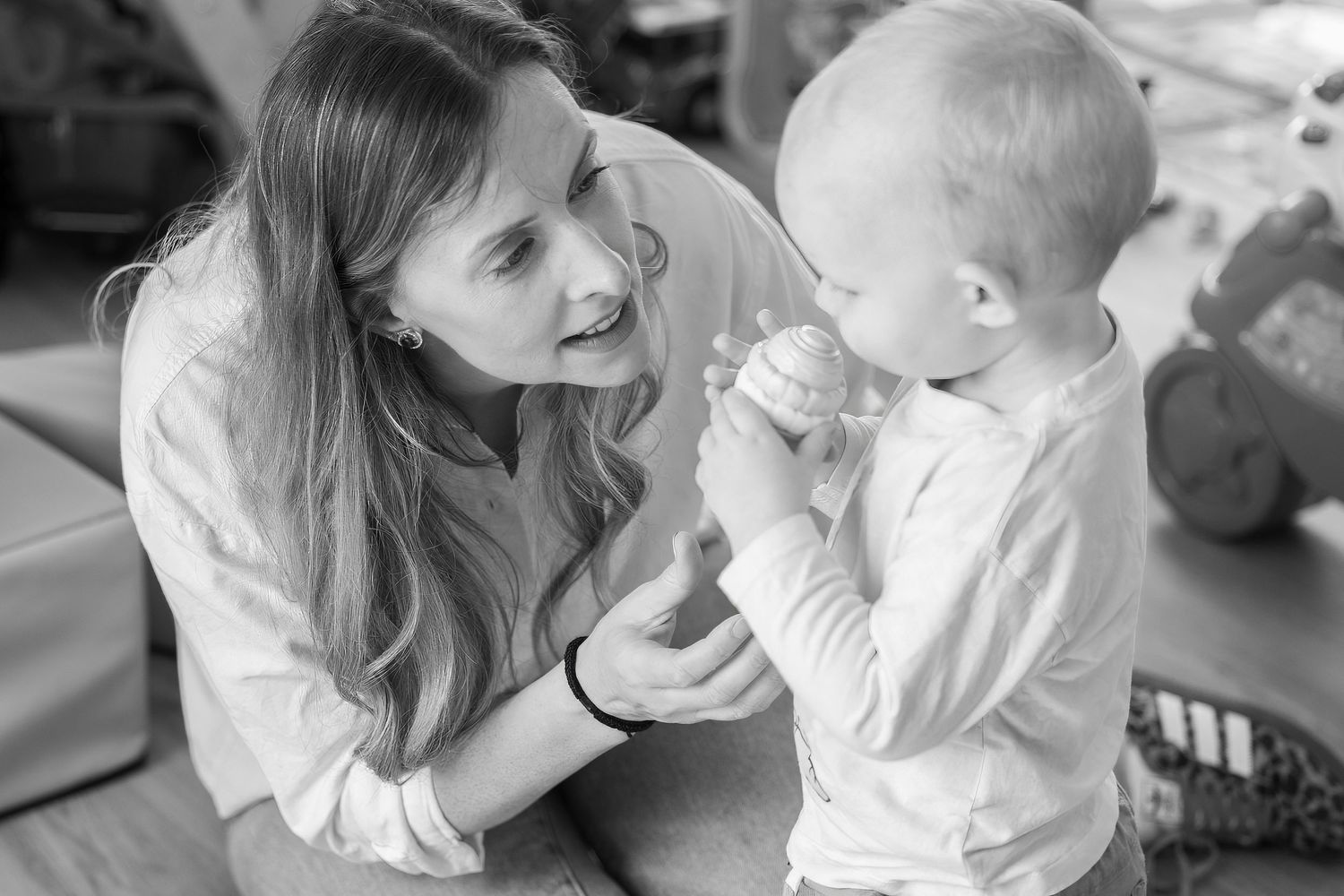Black and white photo of a smiling mother interacting with her baby toddler during playtime at home.