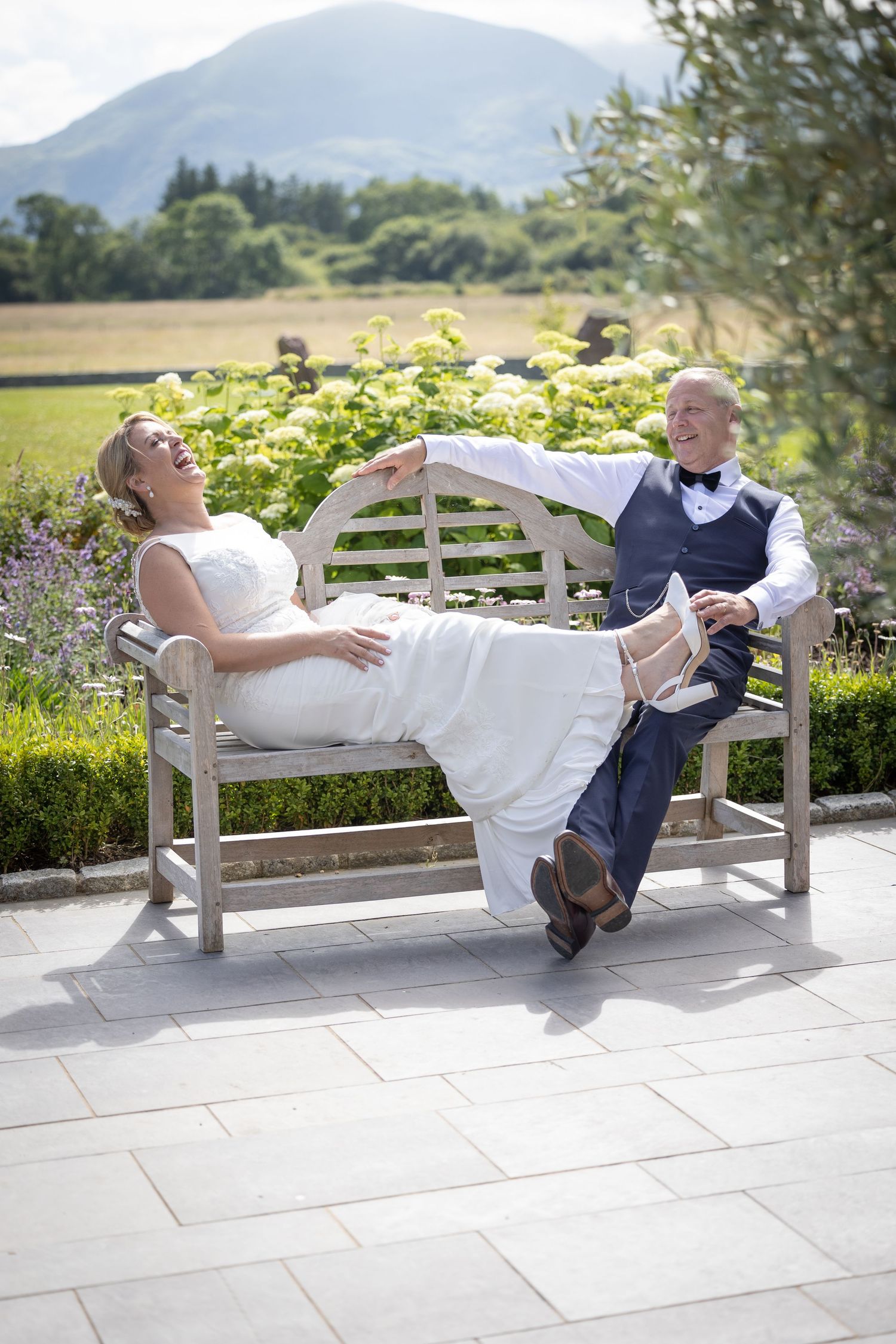 Newlyweds relaxing on white garden bench with mountain view.