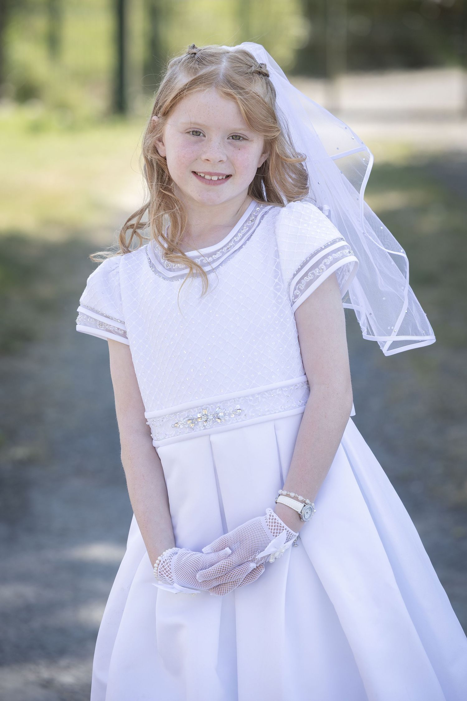 Young person in an elegant white dress posing outdoors for formal photos.