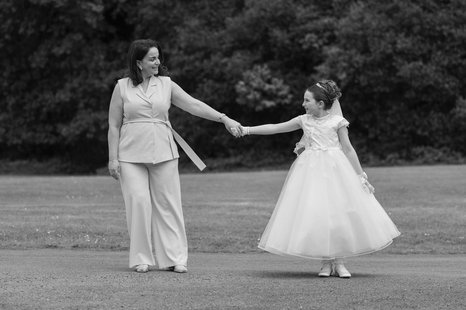 Black and white photo of a woman and young girl in formal attire holding hands and dancing outdoors.