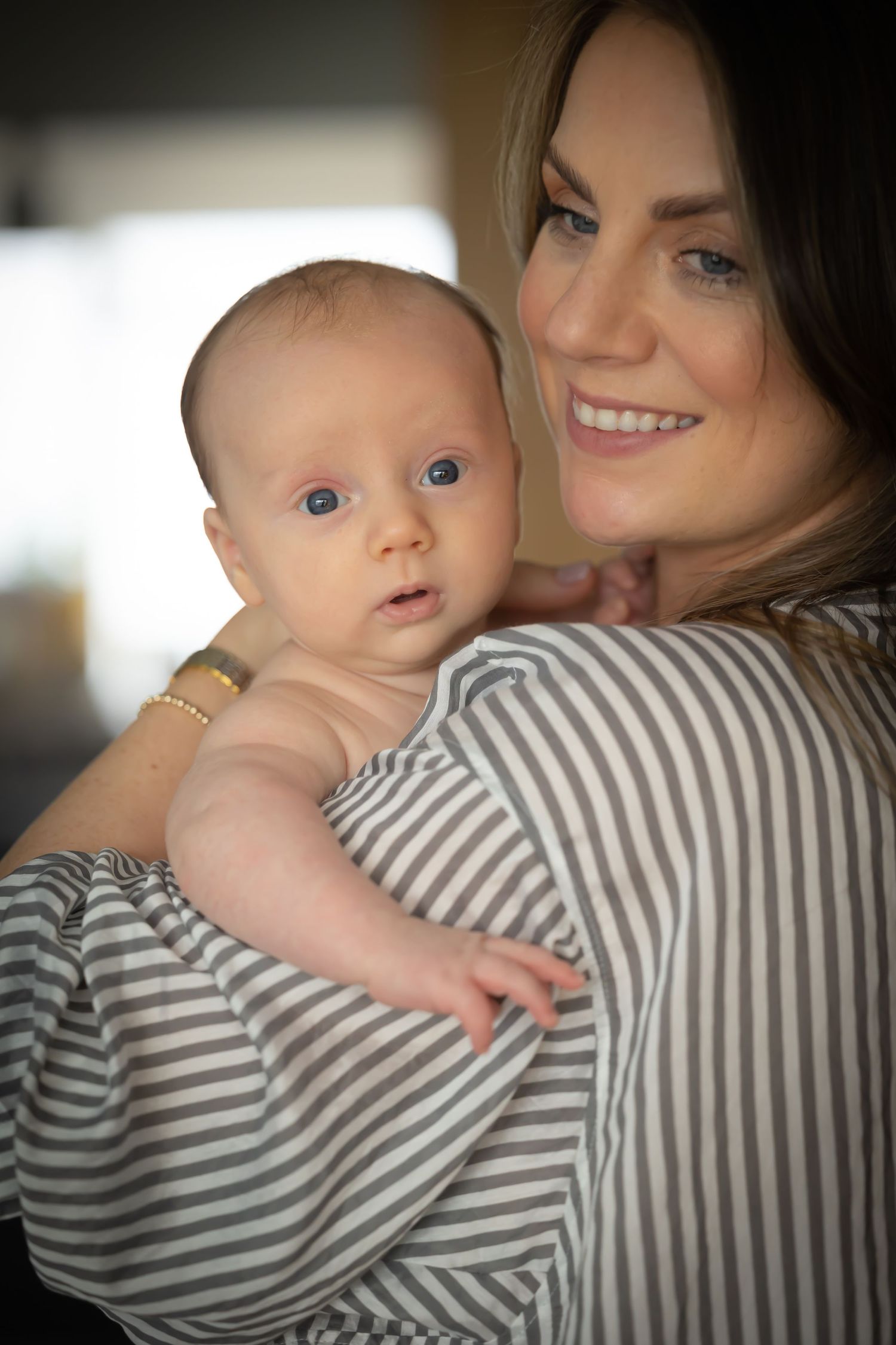 A baby in white clothing reaches up while being held against a striped shirt in a series of candid photos.